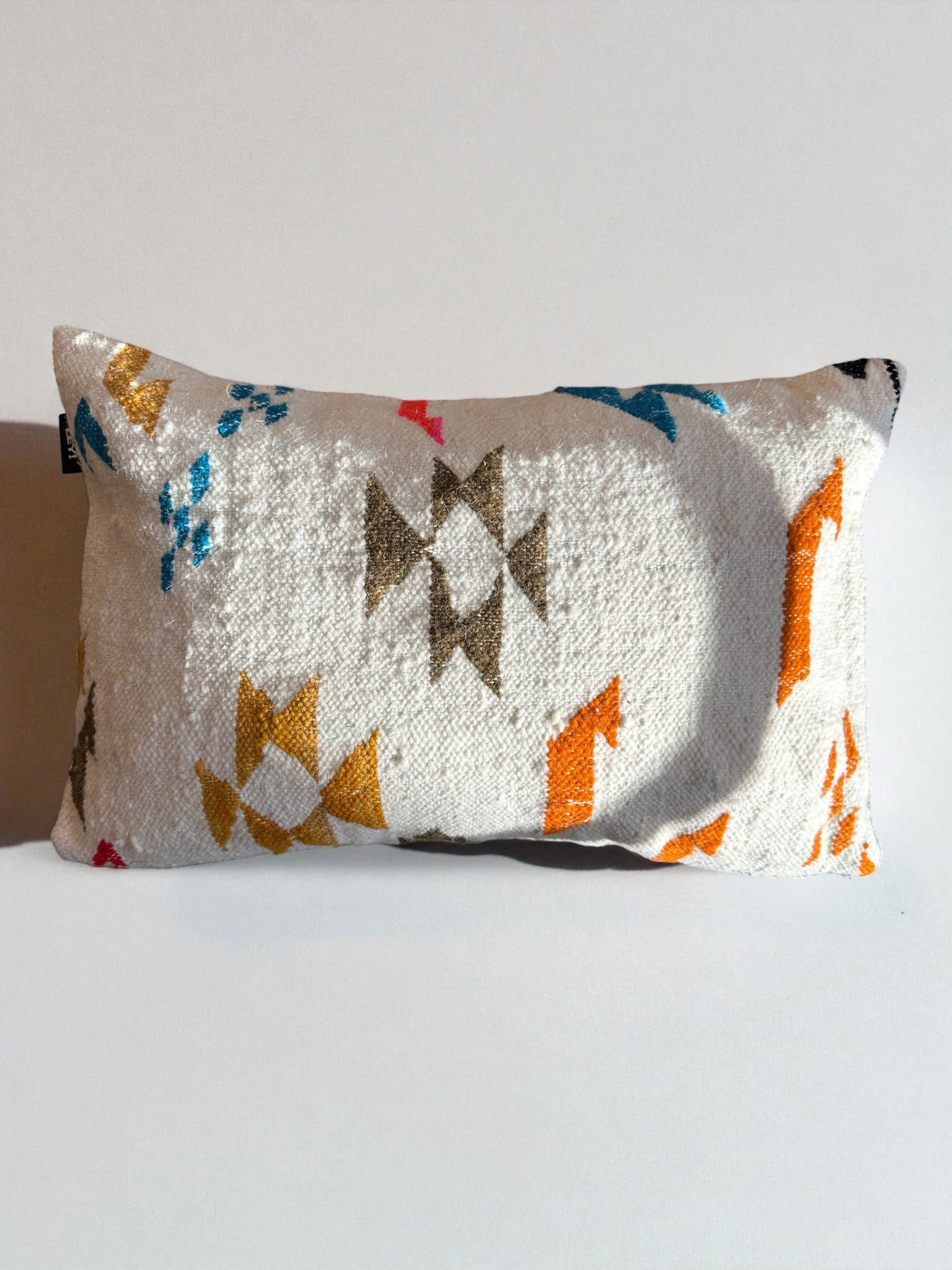 Das LEY! - Kissen - Colorful Line (40 x 60) von LEY! zeichnet sich durch einen weißen, strukturierten Bezug mit gelben, blauen, orangen und braunen geometrischen Mustern aus, die von Marrakesch-Designs inspiriert sind und jedem schlichten, hellen Hintergrund einen einzigartigen Charme verleihen.