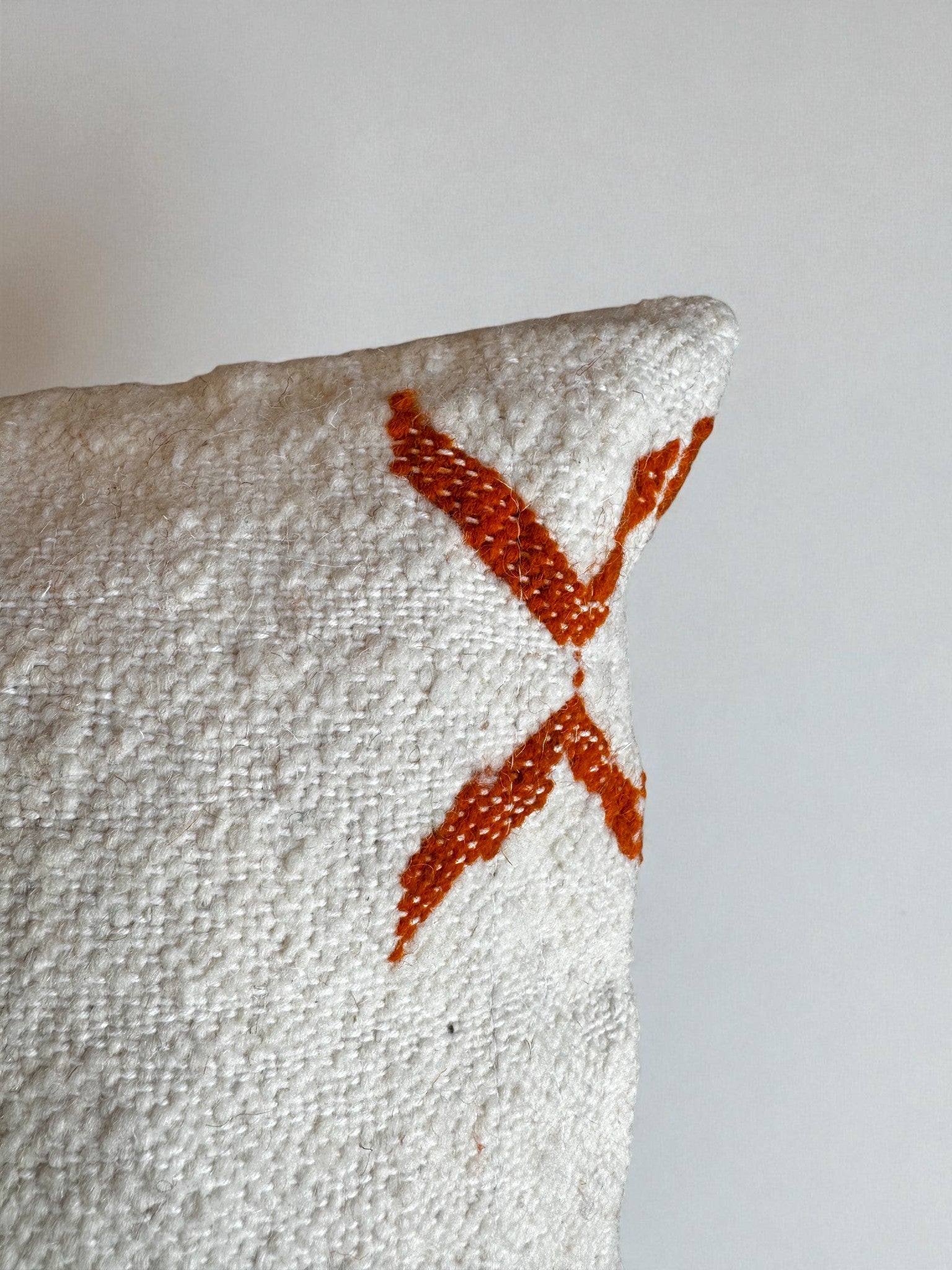 Eine Nahaufnahme des LEY! - Kissen - Colorful Line - 40 x 60 von LEY! mit strukturiertem weißem Stoff und einem auffälligen orangefarbenen "X" in einer Ecke, das auf einem einfarbig weißen Hintergrund abgebildet ist.