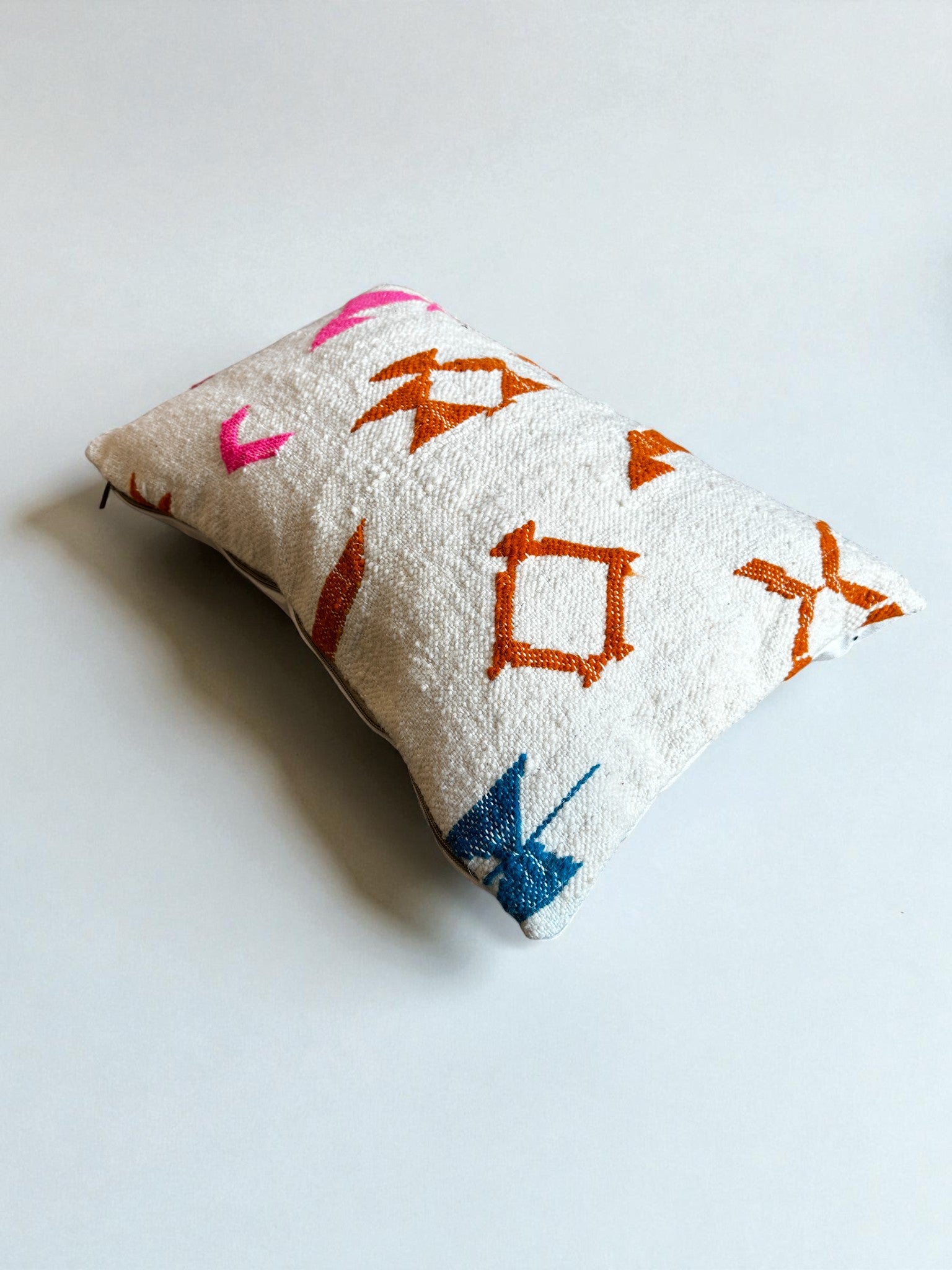 Das LEY! Kissen - Colorful Line (40 x 60) von LEY! besteht aus strukturierter, cremefarbener Schurwolle mit leuchtenden geometrischen Formen in Orange, Pink und Blau, die von der Handarbeit Marrakesch inspiriert sind und einen einzigartigen Charme versprühen.