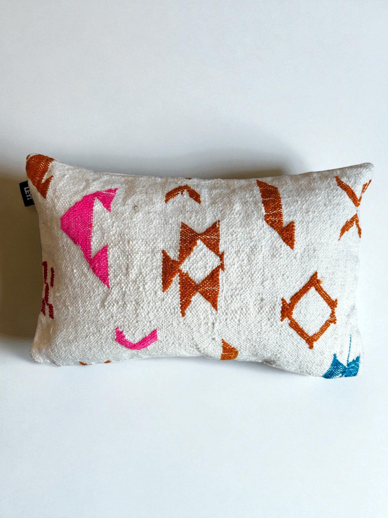 Das LEY! - Kissen - Colorful Line - 40 x 60 ist ein rechteckiges, weißes Kissen mit strukturiertem Stoff und geometrischen Mustern in Orange, Rosa und Blau von LEY! auf einem schlichten, weißen Hintergrund.