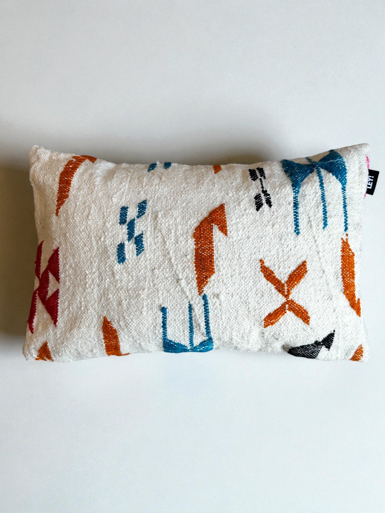 Das LEY! - Kissen - Colorful Line (40 x 60) von LEY! ist ein rechteckiges weißes Kissen mit einer strukturierten Oberfläche und geometrischen Mustern in Orange, Blau, Schwarz und Rot, inspiriert von Marrakesch-Designs und fotografiert auf einem schlichten weißen Hintergrund.