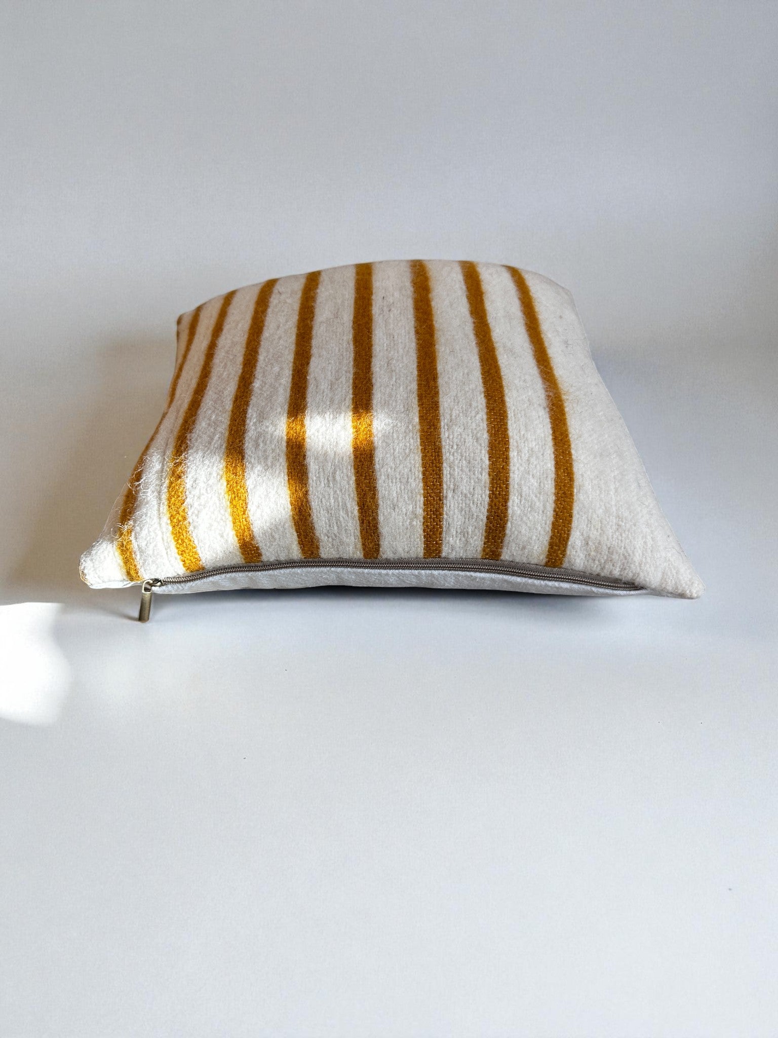 Das Kissen - WINTER EDITION - SONNE - 40x40 von LEY! hat eine quadratische Form mit weißem Hintergrund und vertikalen senfgelben Streifen, die das handgefertigte Marrakesch-Design präsentieren. Es wird auf einer schlichten weißen Fläche bei sanfter Beleuchtung präsentiert.