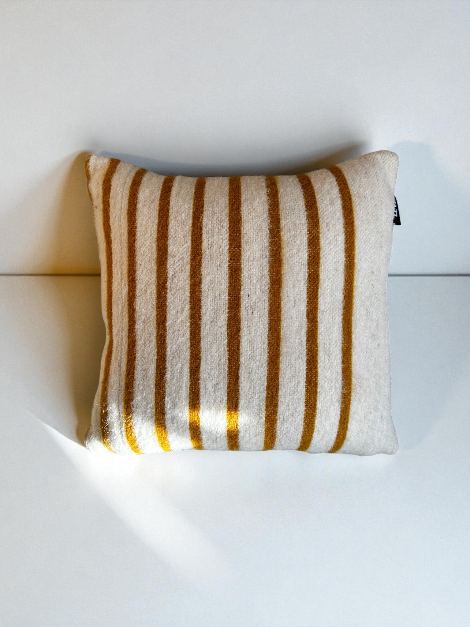 Das Kissen - WINTER EDITION - SONNE von LEY! hat ein 40x40 cm großes, quadratisches Schurwolle-Motiv mit cremefarbenem Hintergrund und vertikalen, senfgelben Streifen - perfekt für gemütliche Wintertage.