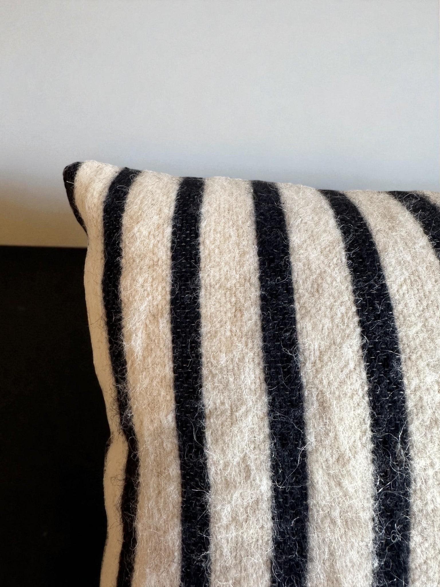 Eine Nahaufnahme des Kissens - WINTER EDITION - TAU - 40 x 40 von LEY! zeigt den strukturierten cremefarbenen Stoff mit vertikalen schwarzen Streifen, handgemacht in Marrakesch, vor einem neutralen Hintergrund.