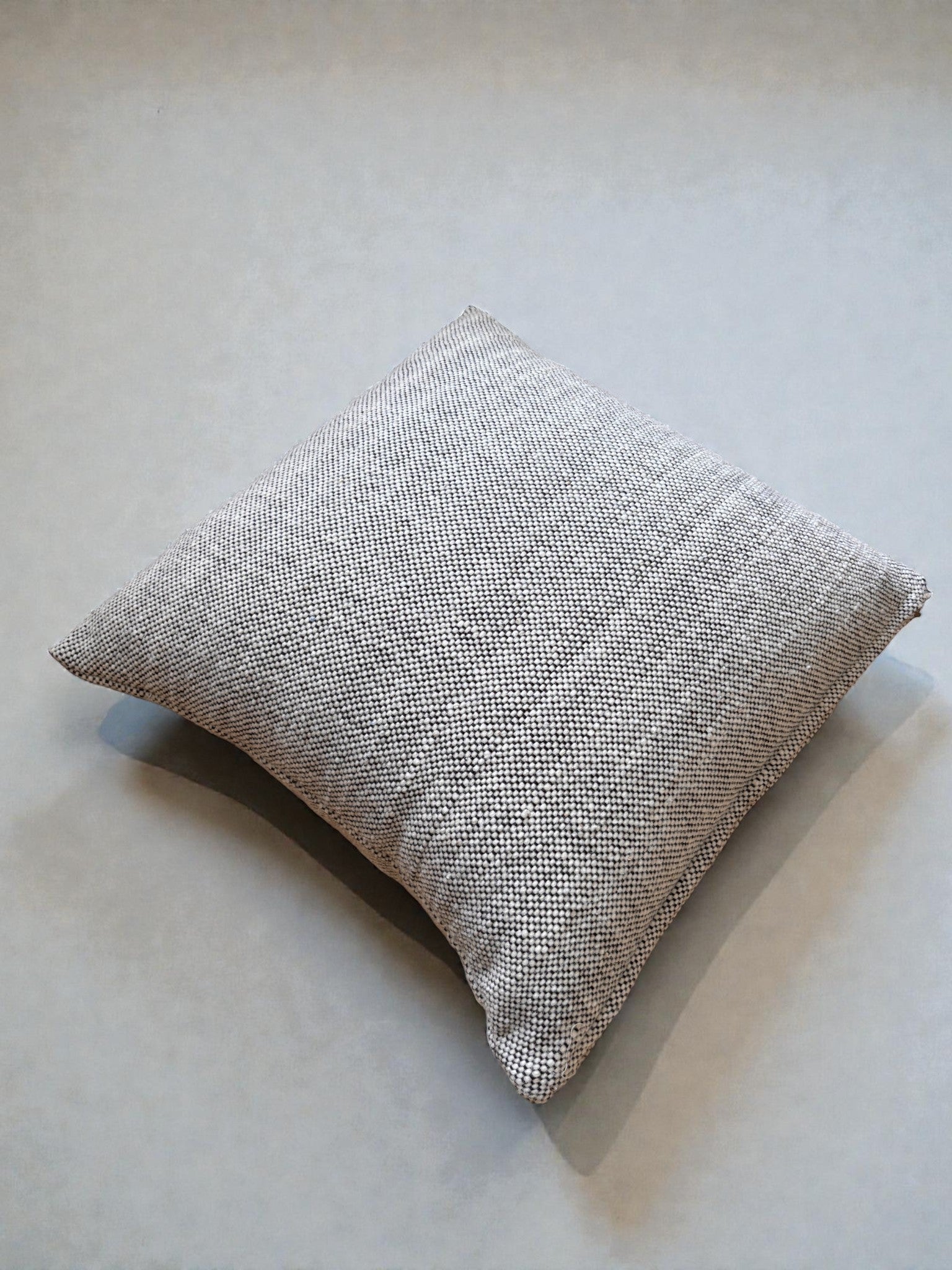 Das Heritage Line Kissen (50 x 50 cm) von LEY! ist ein quadratisches, strukturiertes graues Kissen - ideal als klassisches Sofakissen -, das auf einer glatten, hellen Oberfläche mit einem subtilen Schatten darunter ruht.