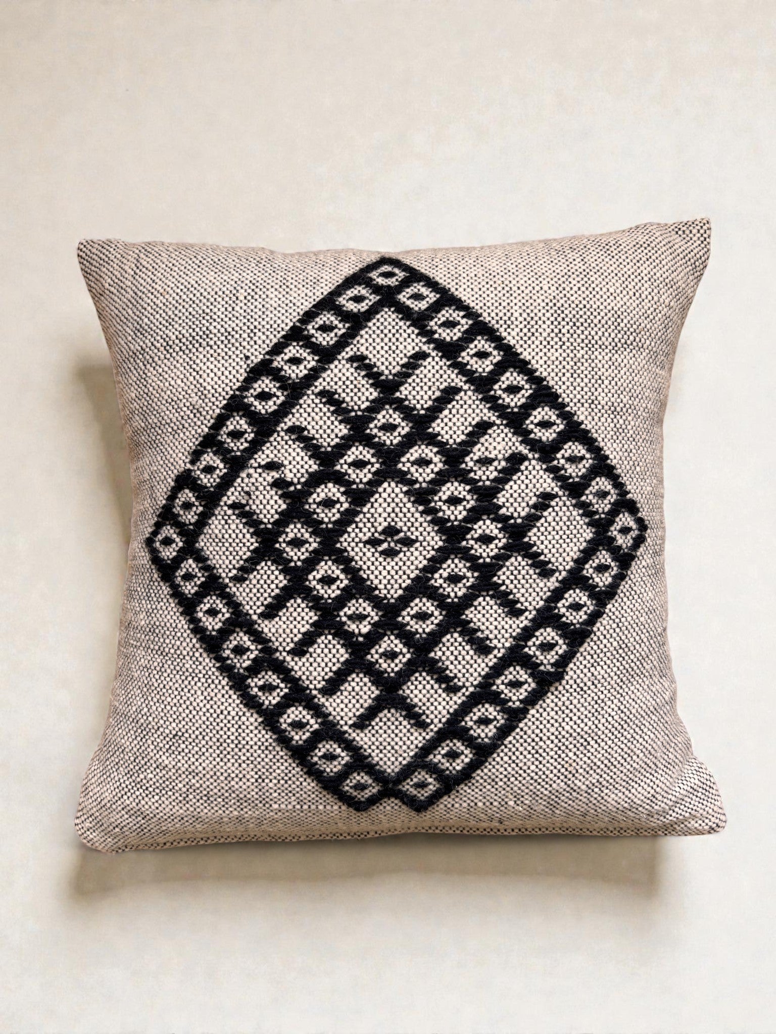 Das LEY! Heritage Line Kissen (50x50 cm) hat einen beigen Strukturstoff mit einem auffälligen schwarzen Rautenmuster, ideal um Ihrem Wohnambiente einen marokkanischen Stil zu verleihen. Präsentiert auf einem einfarbigen, hellen Hintergrund.