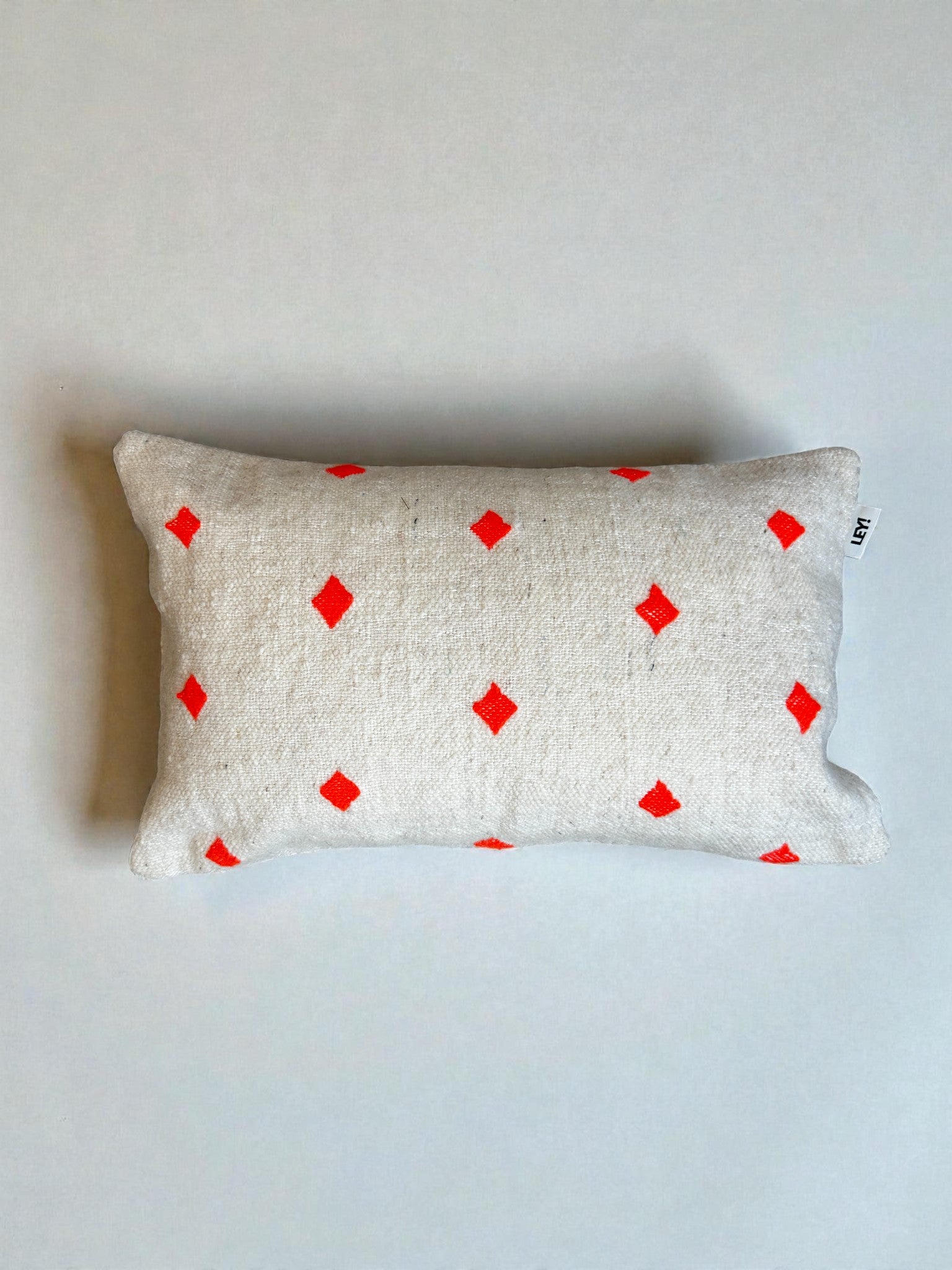 Das LEY! Kissen - Mona Orange - 40 x 60 ist ein rechteckiges Kissen mit strukturiertem Stoff und einem kleinen roten Rautenmuster, das einen Schurwoll-Kissenbezug in Handarbeit im Marrakesch-Stil zeigt, der auf einem schlichten hellen Hintergrund abgebildet ist.