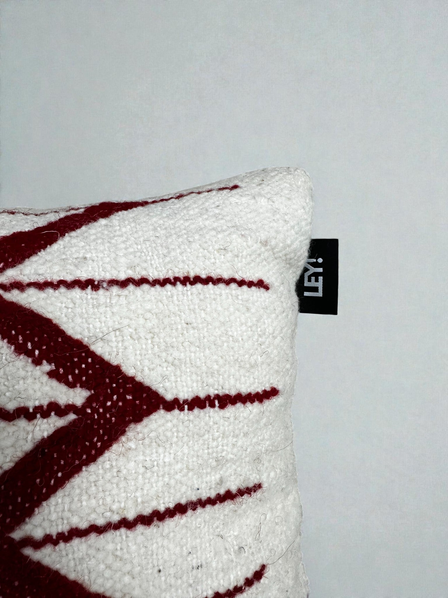 Nahaufnahme des LEY! Kissen - Colorful Line (30x40) von LEY!, das ein rotes Zickzack-Muster auf einer weißen Wand zeigt.