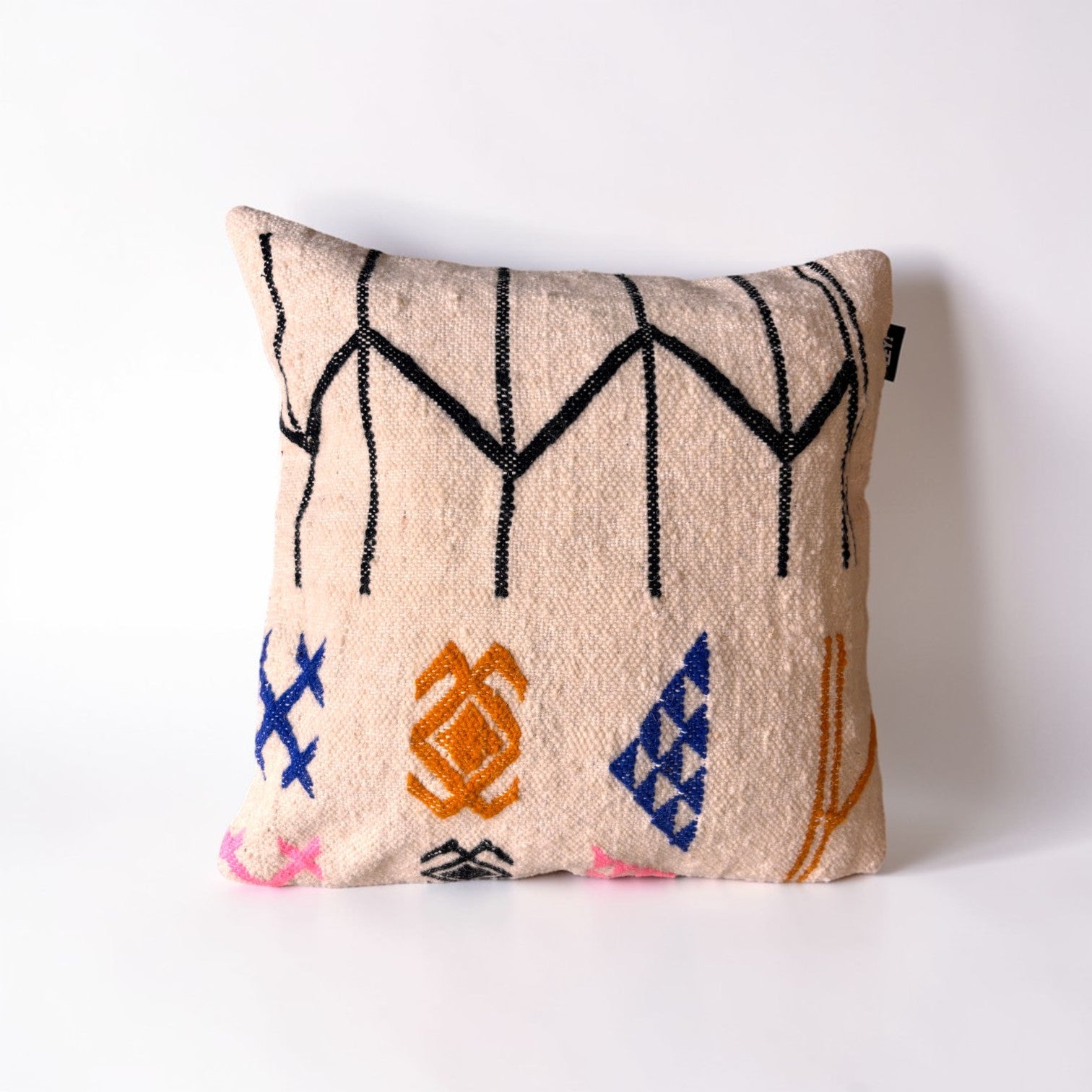 Das LEY! Kissen - Colorful Line (50 x 50) von LEY! ist ein beiges Schurwolle-Kissen mit schwarzer, blauer, oranger und rosa geometrischer Stickerei, handgemacht Marrakesch, auf weißem Hintergrund.