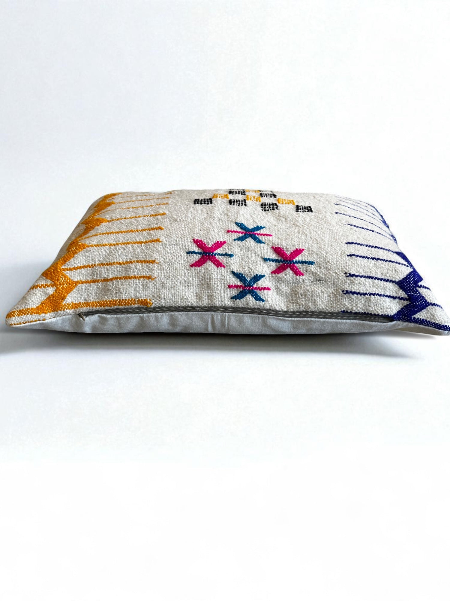 Das LEY! Kissen - Colorful Line (40 x 60) von LEY! ist ein rechteckiges Schurwolle-Kissen mit weißer Basis und bunten, handgefertigten Marrakesch-inspirierten Mustern in Gelb, Pink, Blau und Schwarz. Flach auf weißem Hintergrund liegend.