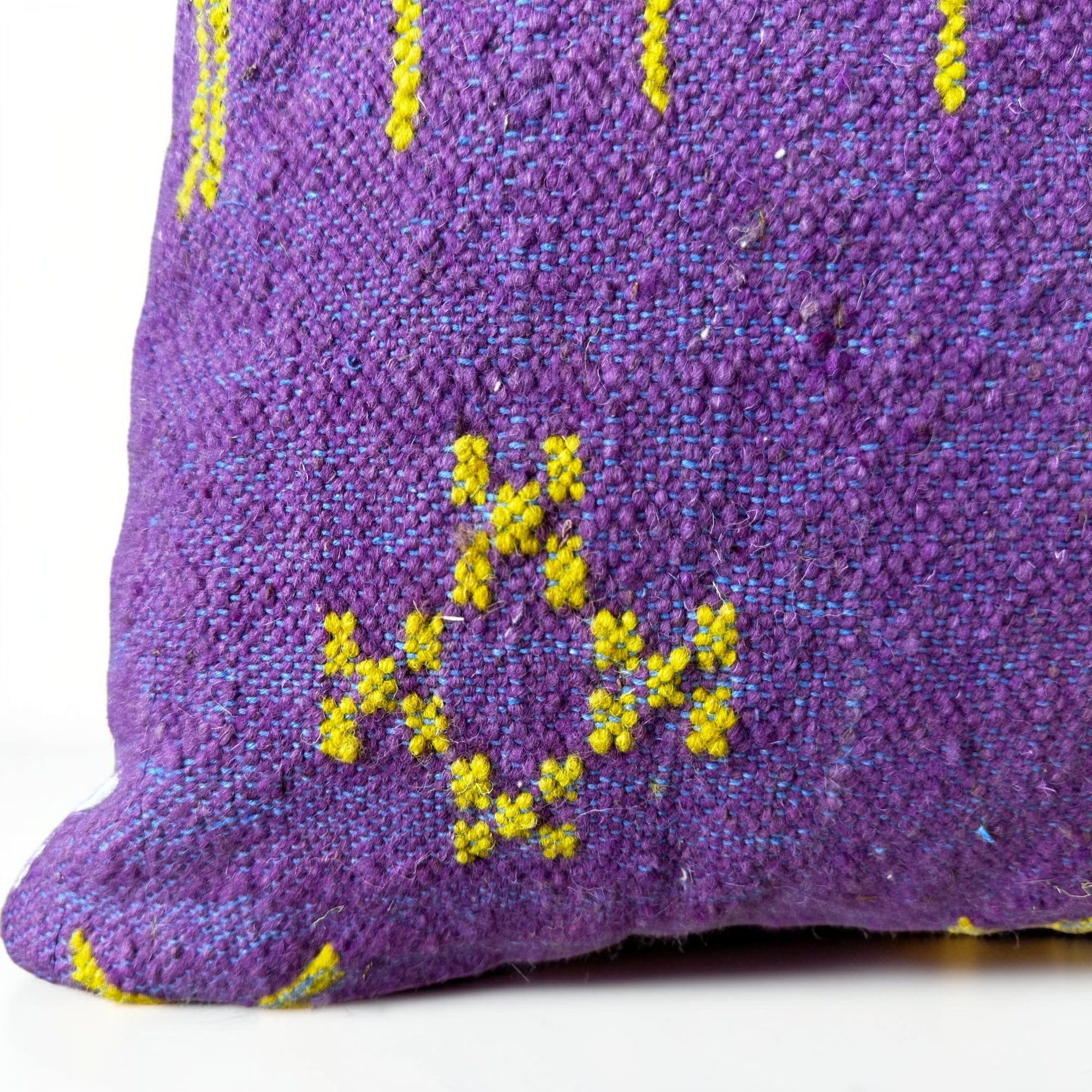 Nahaufnahme eines gewebten lilafarbenen Stoffes mit einem gelben geometrischen Muster, das X-förmige Stiche und Rauten aufweist - wahrscheinlich Teil des LEY! Kissen - Colorful Line - LILA EDITION - 50x50 Zierkissen von LEY!.
