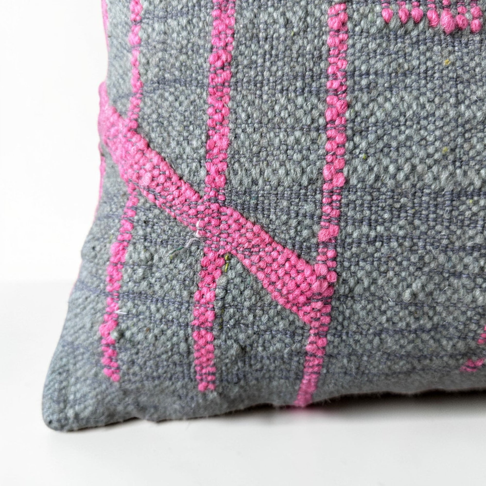 Nahaufnahme des LEY! Kissen - Colorful Line - SAGE EDITION (50x50) von LEY! mit grauer Schurwolle mit leuchtend rosa geometrischen Linien, handgefertigt in Marrakesch, vor einem schlichten weißen Hintergrund.