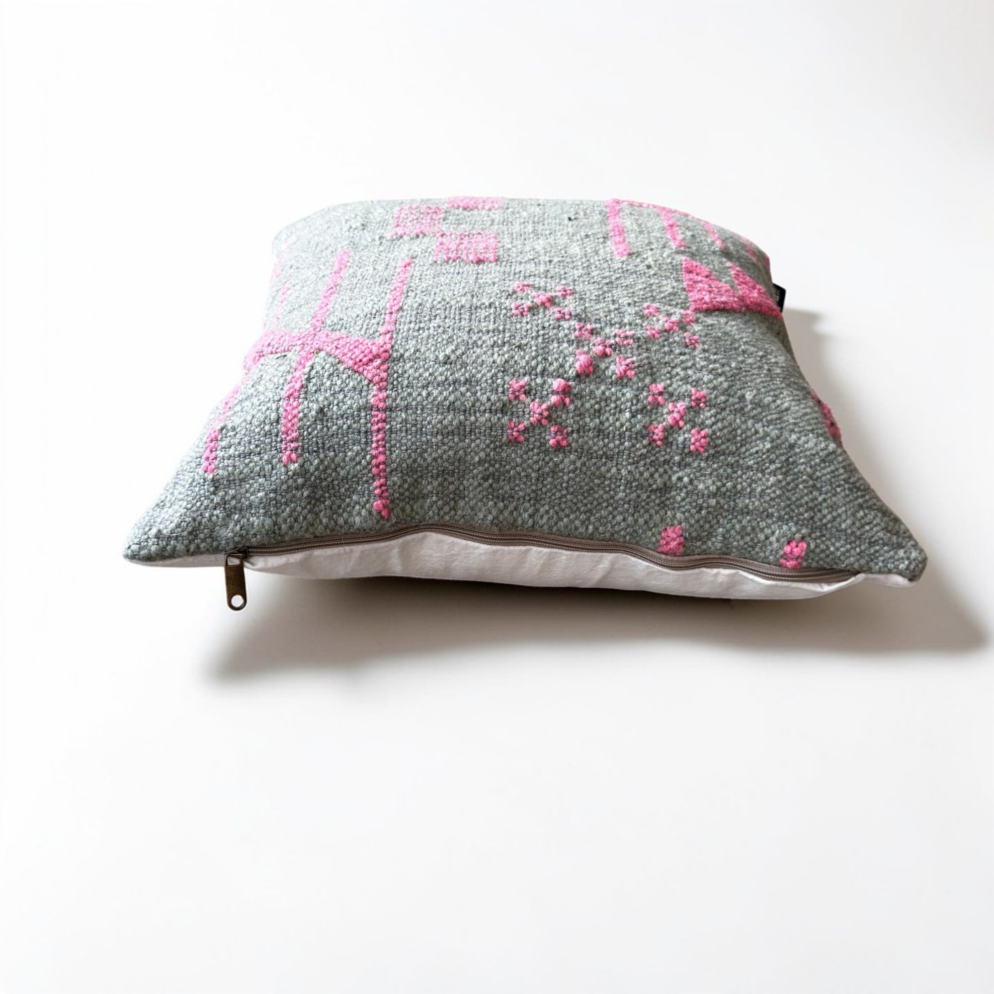 Das LEY! Kissen - Colorful Line - SAGE EDITION (50x50) von LEY! ist ein graues Kissen mit rosa geometrischen und floralen Stickmustern, einem sichtbaren Reißverschluss und liegt auf einer weißen Oberfläche. Dieses handgefertigte Stück aus Marrakesch vereint Stil und Handwerkskunst.