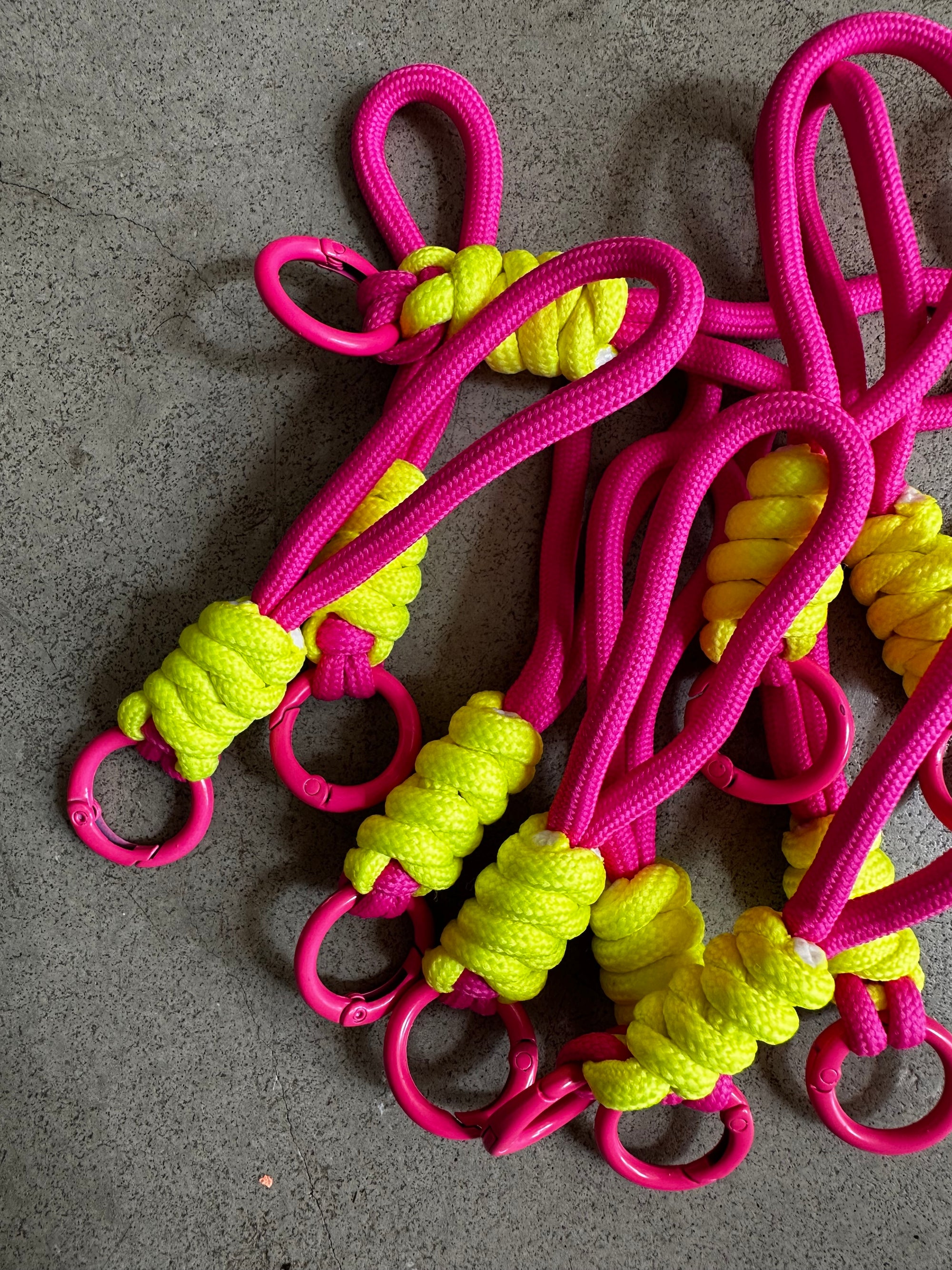 Mehrere LEY! Schlüsselanhänger - neongelb-pink mit gelben Kordelwickeln und pinken Karabinerclips sind auf einer grauen Oberfläche abgebildet - perfekt für Taschen oder Schlüsselanhänger.