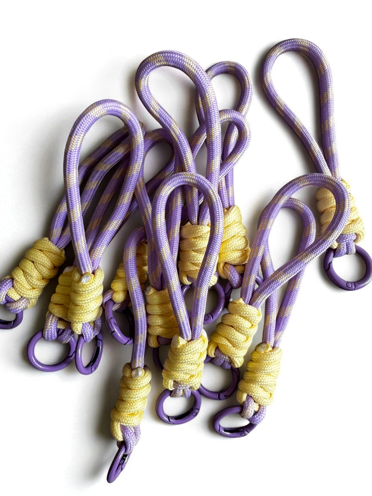 Ein Set von LEY! Schlüsselanhänger - gelb-lila, mit lilafarbenem und gelbem Paracord mit Schlaufen, gelber Umwicklung und lilafarbenen Metallringen, auf weißem Untergrund. Ideal als Taschen-Accessoires oder stylische Schlüsselanhänger.