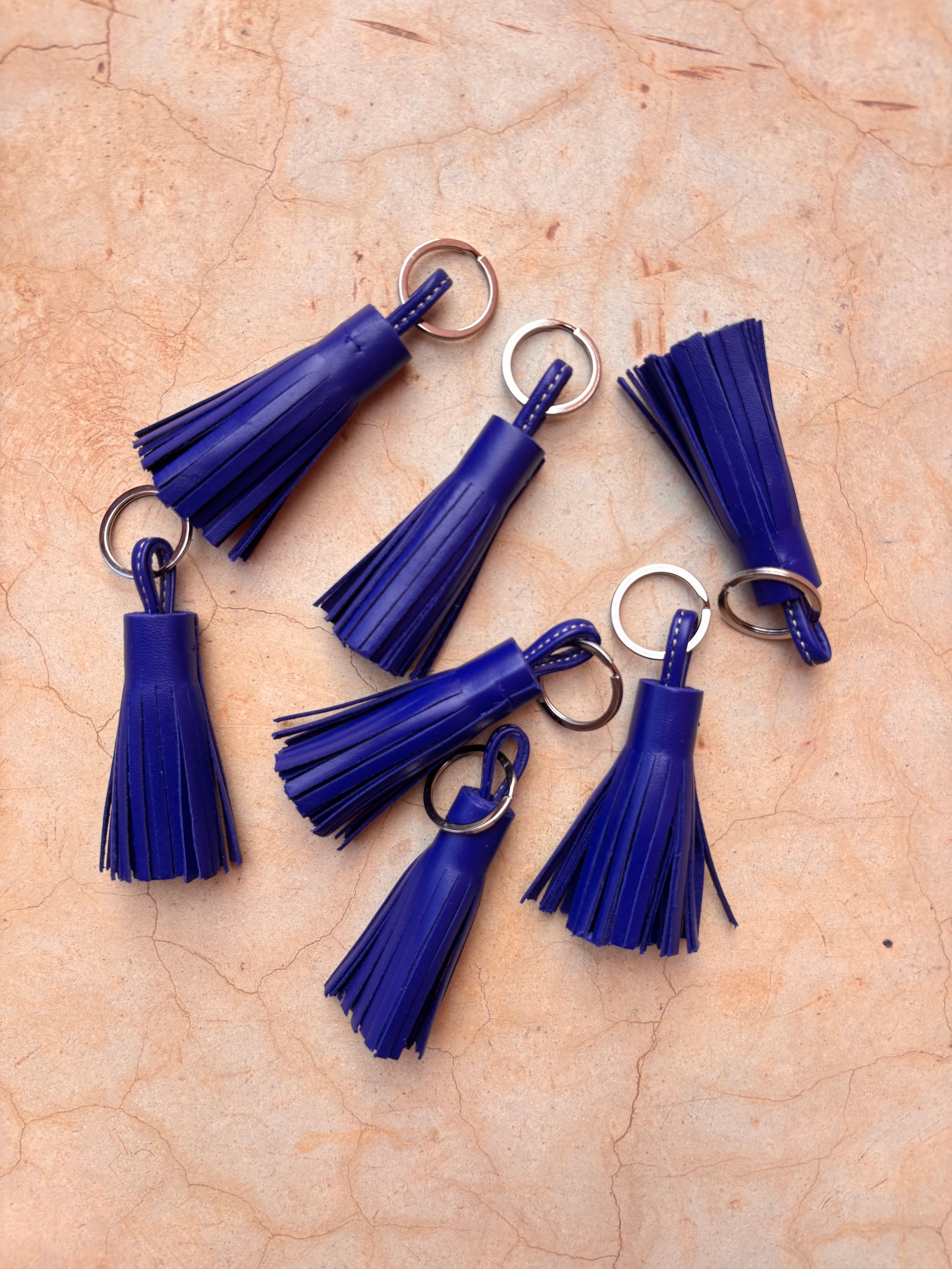 Sechs LEY! Leder-Schlüsselanhänger - dunkelblau - mit silbernen Ringen liegen locker auf beigem Marmor. Die stilvollen Accessoires sind ideale Geschenkideen und dekorativ angeordnet.