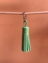 Der von LEY! gefertigte Leder-Schlüsselanhänger in mintgrün mit kleiner Quaste hängt an einem pinken Band vor pfirsichfarbenem Hintergrund - eine stilvolle Geschenkidee.