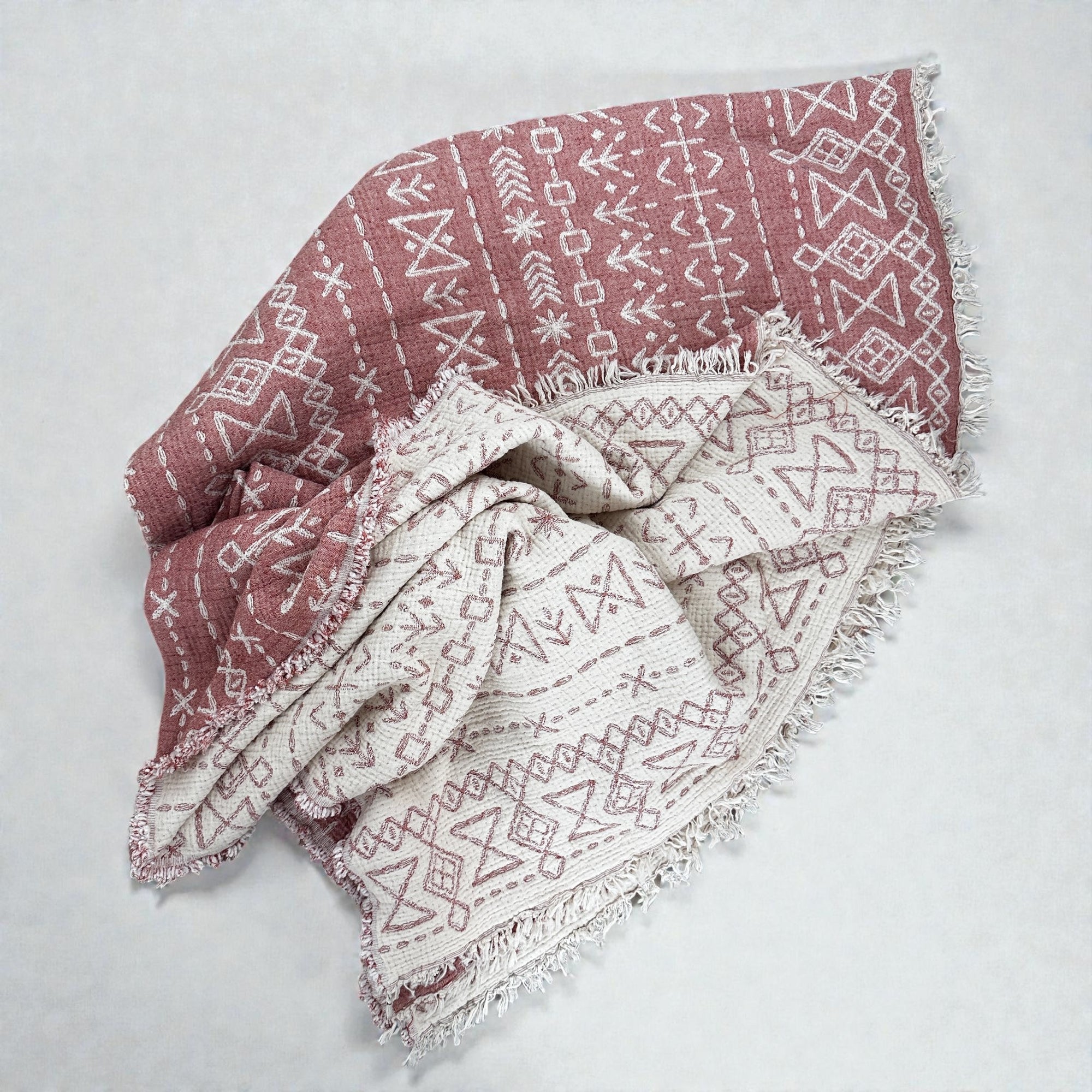 Die LEY! CALMA Musselin Decke in Rotbraun-Weiß (1,60 x 2,30 m) zeichnet sich durch geometrische Boho-Muster und ausgefranste Kanten aus. Der weiche, atmungsaktive Stoff sorgt für Stil und Komfort, wenn er auf einer leichten Oberfläche liegt.