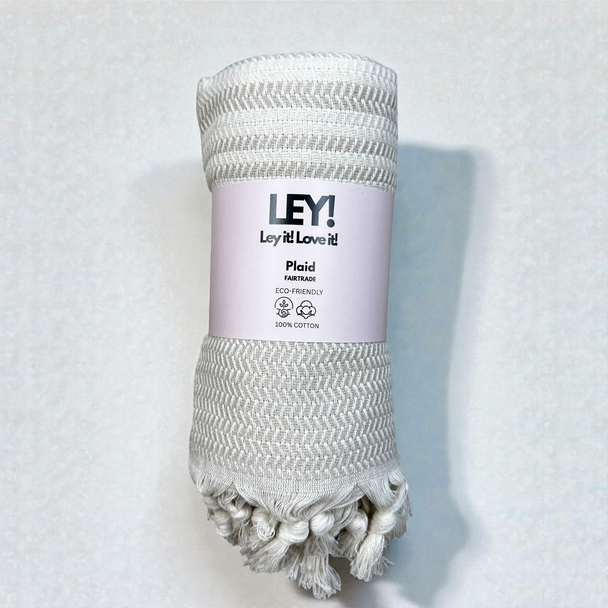 Die LEY! Plaid - Zickzack - Beige ist eine beigefarbene Baumwolldecke mit dezentem Chevron-Muster und stilvollen Fransen. Mit der Aufschrift "LEY! Lay it! Love it!" ist sie fair gehandelt, umweltfreundlich, 100% Baumwolle - perfekt als Picknickdecke oder Saunatuch.