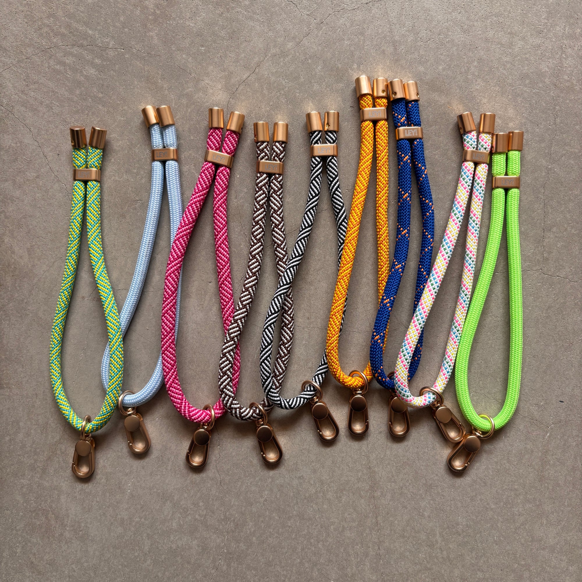 Eine Reihe von LEY! Schlüsselanhänger - Gelb - Türkis mit goldenen Clips und Kappen, mit einzigartigen Flechtmustern, übersichtlich präsentiert - perfekt als Handykette oder Lanyard Handyband für stilvolles Handy Zubehör.