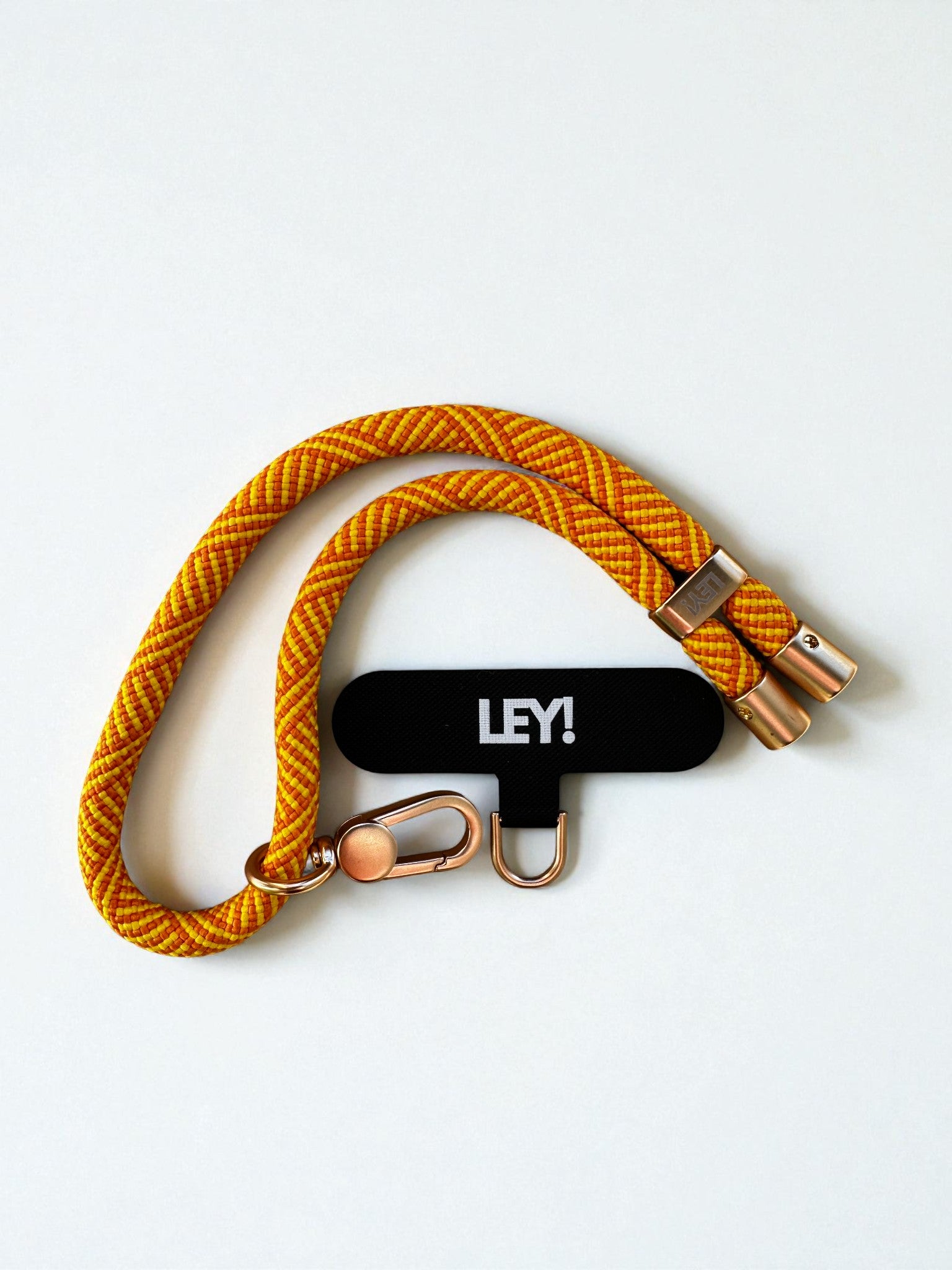 Ein gelber und orangefarbener Schlüsselanhänger von LEY! mit goldenen Metallspangen ist auf weißem Hintergrund arrangiert, daneben ein schwarzer LEY!-Anhänger in fetten weißen Buchstaben - stilvoll und perfekt, um Ihre Schlüssel griffbereit zu halten.