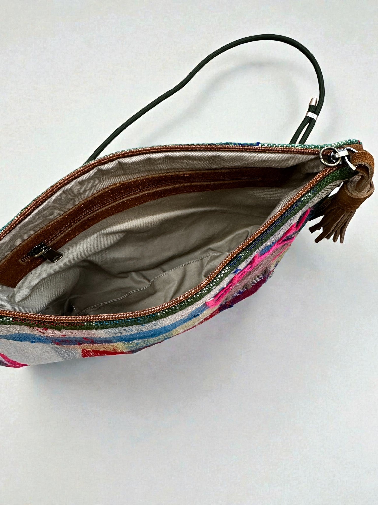 Die LEY! Tasche - OCULIA CLUTCH von LEY! ist eine kleine Clutch mit Reißverschluss, einer bunt gemusterten Außenseite, beigem Innenfutter, einer Innentasche mit Reißverschluss und einem Handgelenkriemen mit Quaste - perfekt, um urbanes Design zu präsentieren. Die Tasche ist offen und von oben betrachtet.
