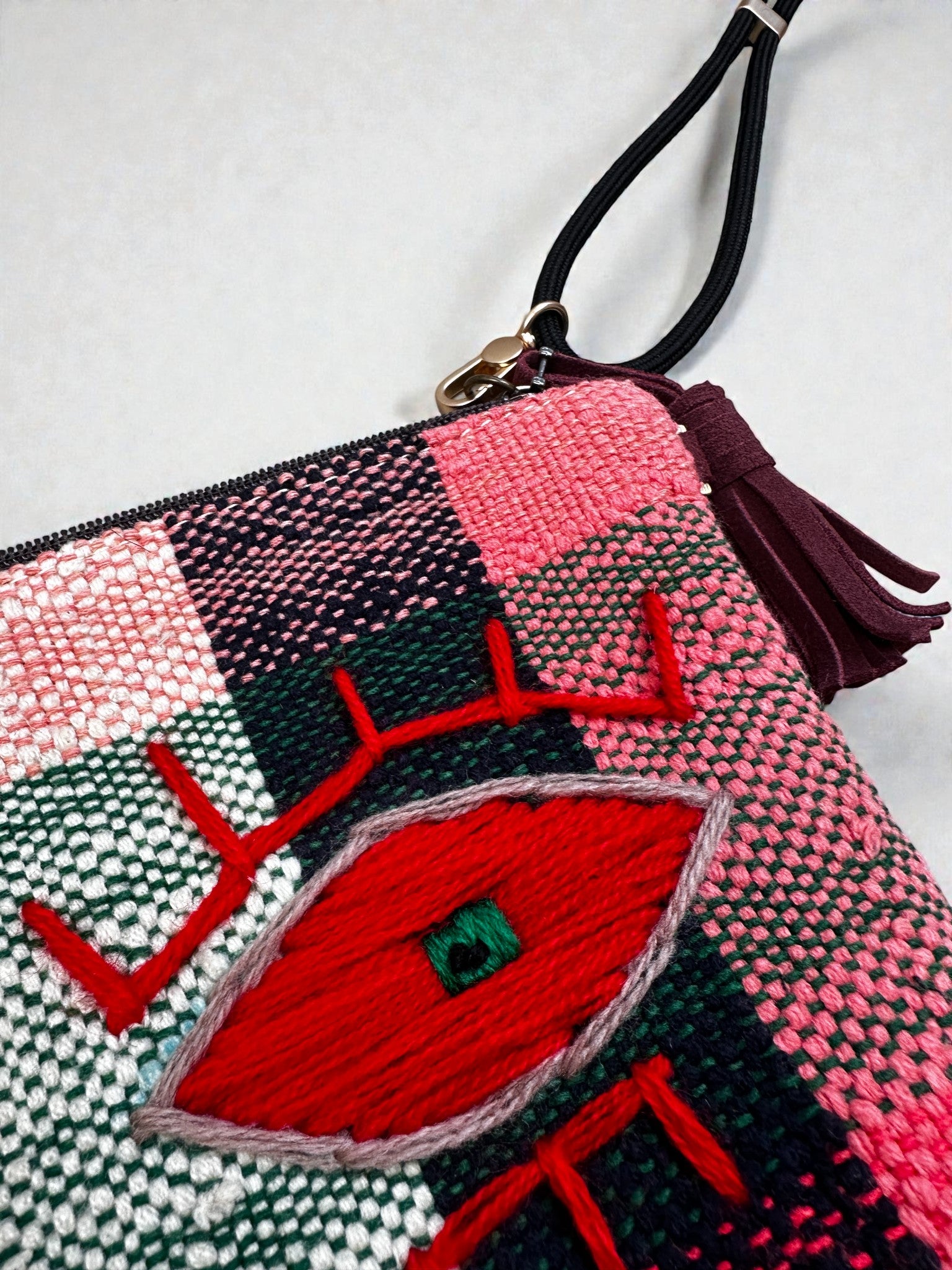 Die LEY! Tasche - OCULIA CLUTCH von LEY! ist eine handgewebte, karierte Clutch in Rosa, Grün und Weiß mit roter Augenstickerei, die mit einem Reißverschluss und einer dunklen Quastenschlaufe für Vintage-Flair sorgt.