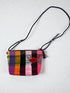 Die LEY! Tasche - OCULIA CLUTCH von LEY! ist eine farbenfrohe, handgefertigte Umhängetasche mit schwarzem, verstellbarem Riemen, Karomuster in Gelb-, Orange-, Grün-, Pink- und Lila-Tönen und gesticktem Augenmotiv.