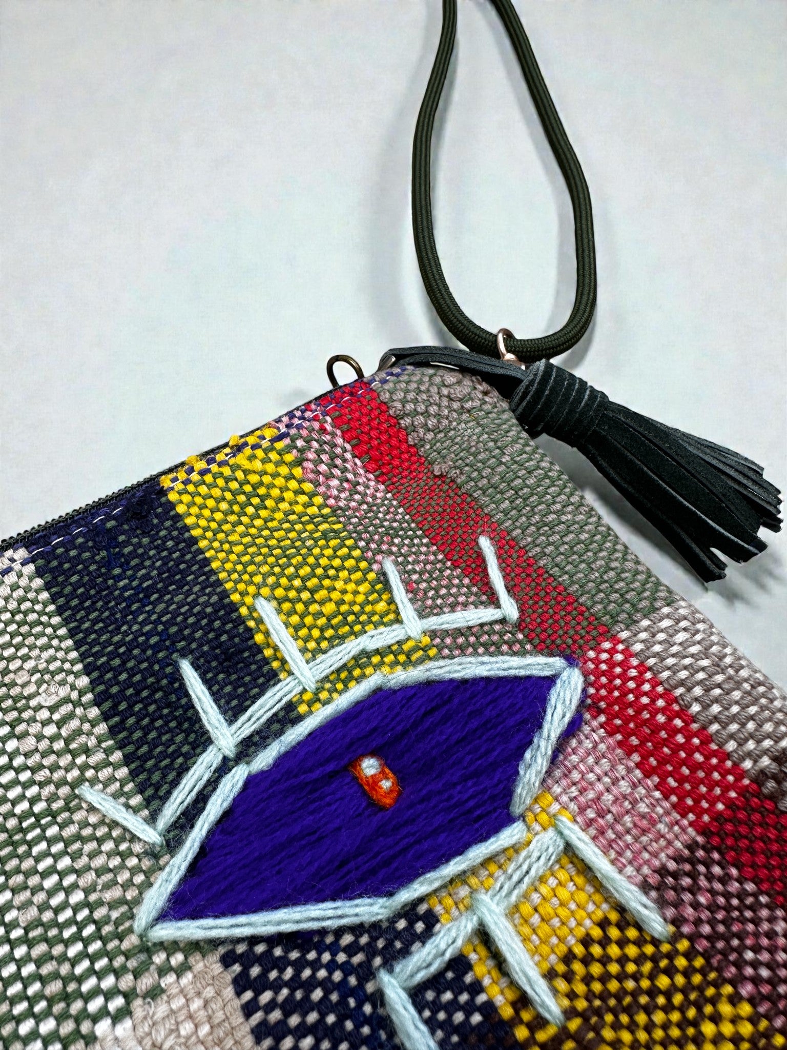 Die LEY! Tasche - OCULIA CLUTCH von LEY! ist eine farbenfrohe Tasche mit gestreiftem Vintage-Stoff, einem großen blauen gestickten Auge mit weißen Wimpern, sowie einem schwarzen Handgelenkband und einem Schlüsselanhänger mit Quaste für einen auffälligen Stil.