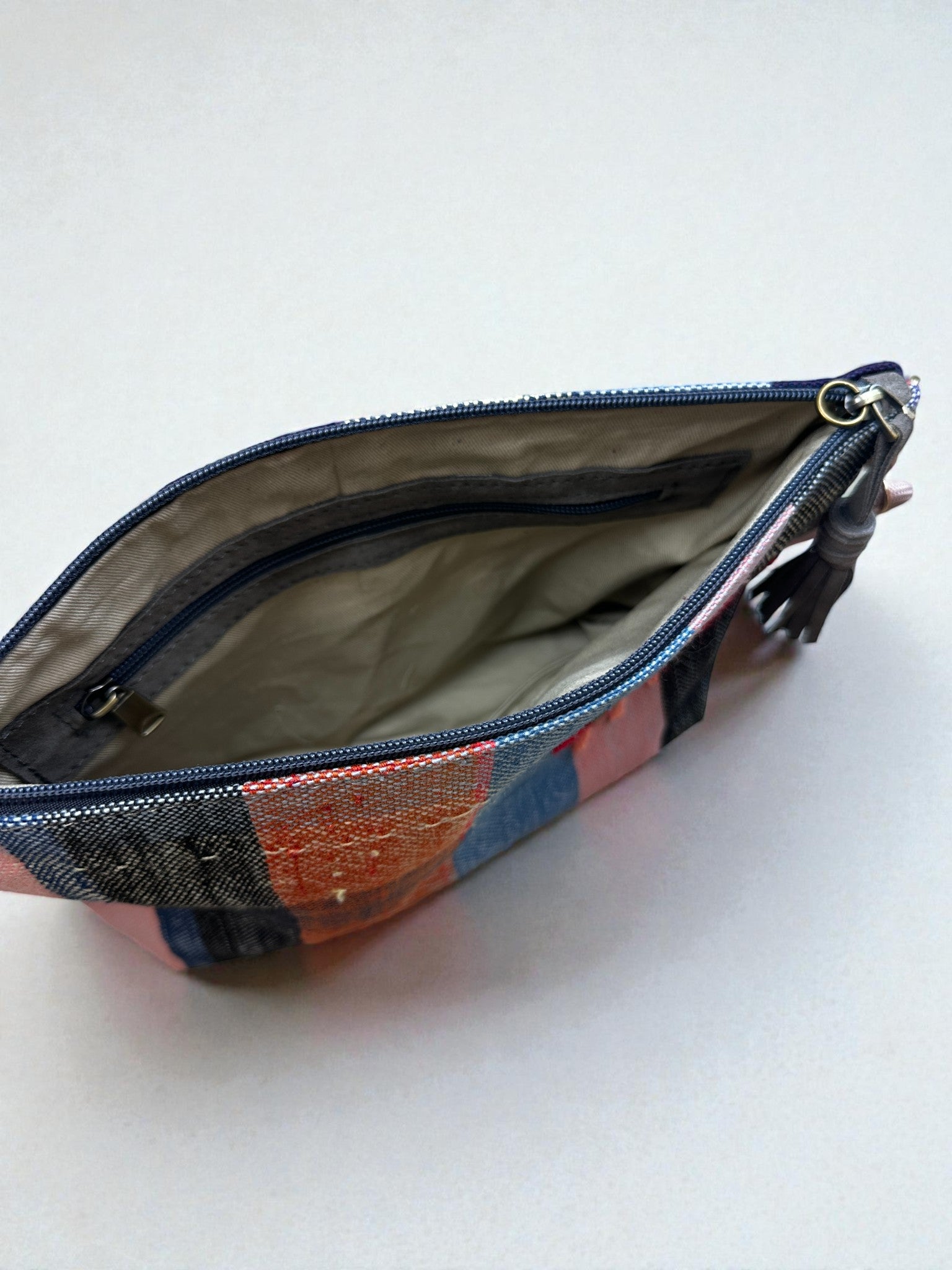 Die LEY! Tasche - OCULIA CLUTCH von LEY! ist eine kleine Clutch mit Reißverschluss, einer Außenseite aus Patchwork-Vintage-Stoff, hellem Futter, einer Innentasche und einer dekorativen Quaste am Reißverschluss.