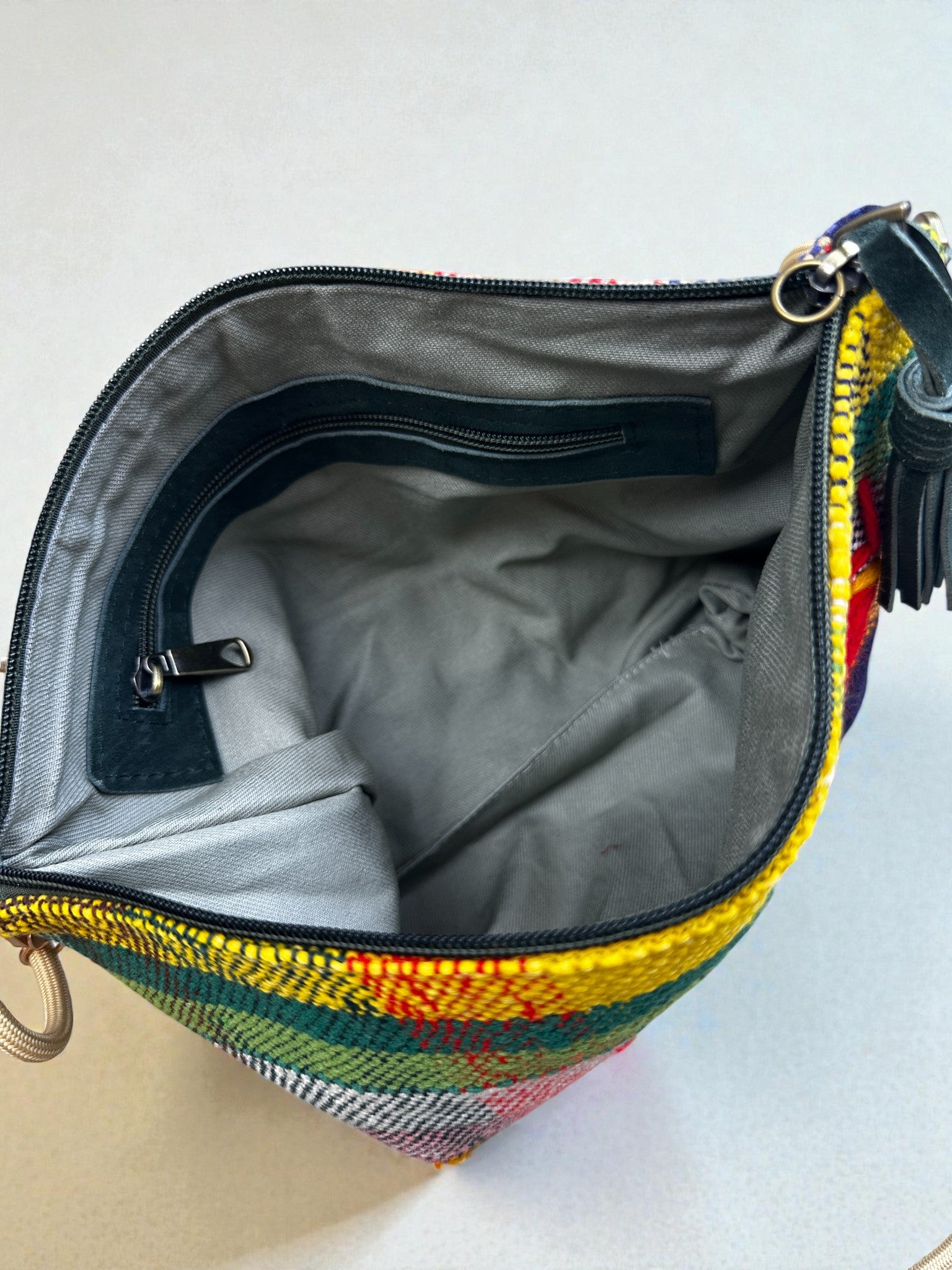 Öffnen Sie die LEY! Tasche - OCULIA CLUTCH von LEY! und enthüllt ein graues Innenfach mit einem Reißverschluss- und einem offenen Fach. Das kompakte Design hat ein gelbes, rotes und grünes gewebtes Äußeres und einen dunklen Reißverschluss auf dem Deckel.