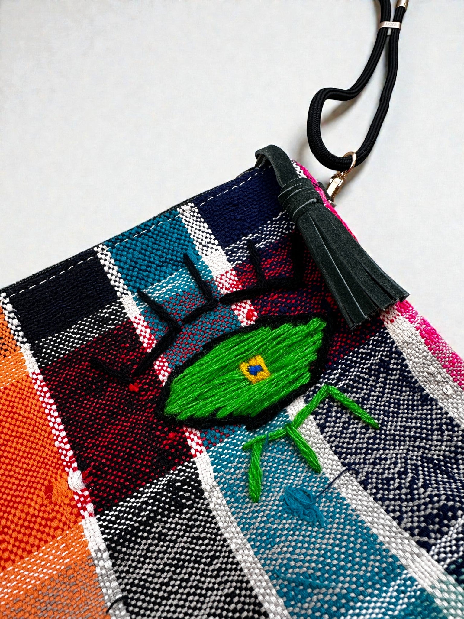 Die LEY! Tasche - OCULIA CLUTCH von LEY! ist eine lebhaft karierte Stofftasche mit grünem Quasten-Reißverschluss und einem gestickten grünen Auge, die jedem Outfit Vintage-Flair verleiht.