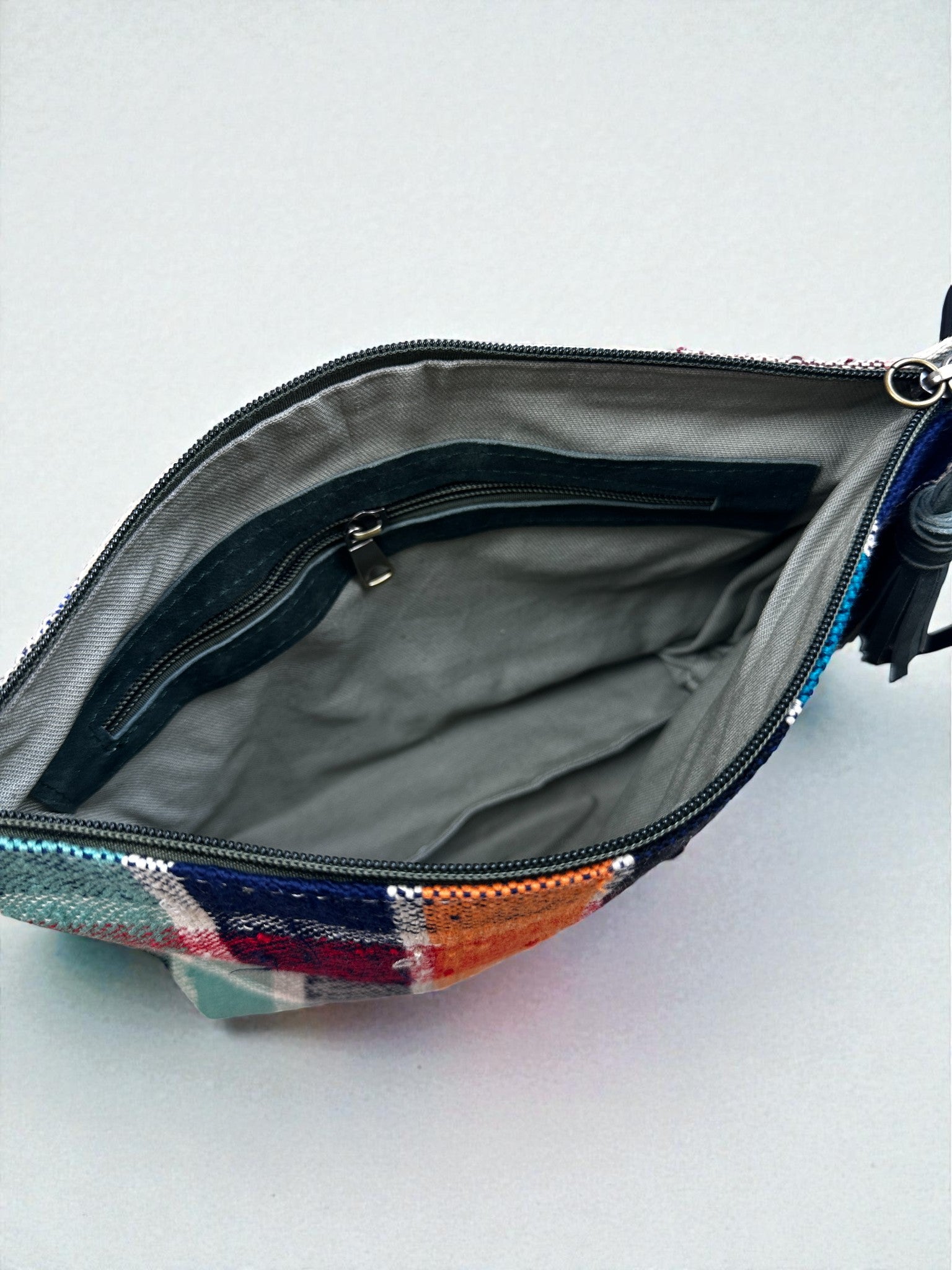 Offener Blick auf die LEY! Tasche - OCULIA CLUTCH von LEY!: eine farbenfrohe Handtasche aus kariertem Stoff mit grauem Futter, Hauptfach und Innentasche mit Reißverschluss. Diese handgefertigte Clutch ist von Vintage-Stoffen inspiriert und wird leer auf einer hellen Oberfläche gezeigt.