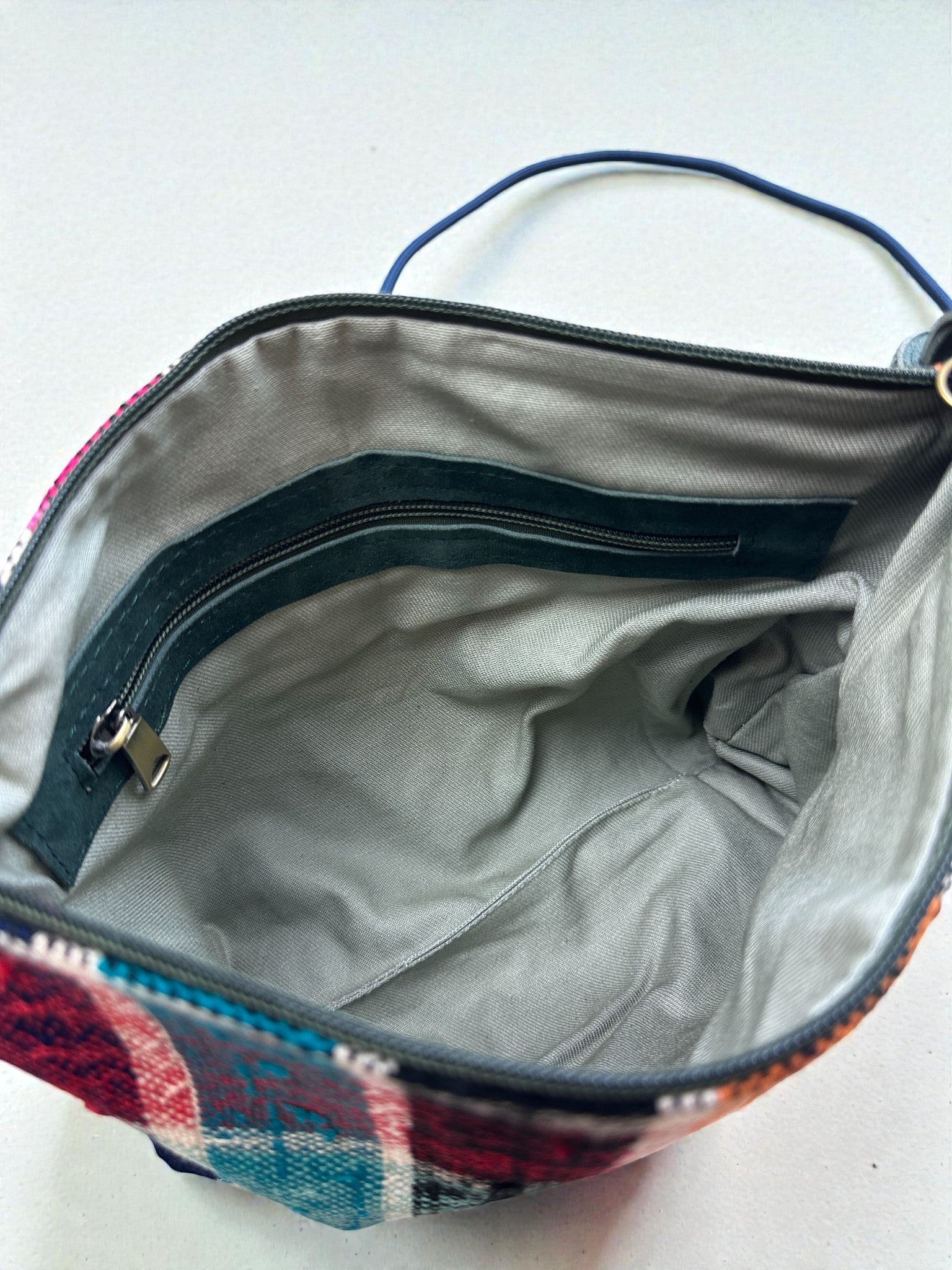 Eine Nahaufnahme der LEY! Tasche - OCULIA CLUTCH von LEY! zeigt ihr Stofffutter, die Innentasche mit Reißverschluss, den Henkel und die karierte Außenseite am Rand. Diese handgefertigte Umhängetasche kombiniert Stil und praktisches Design.
