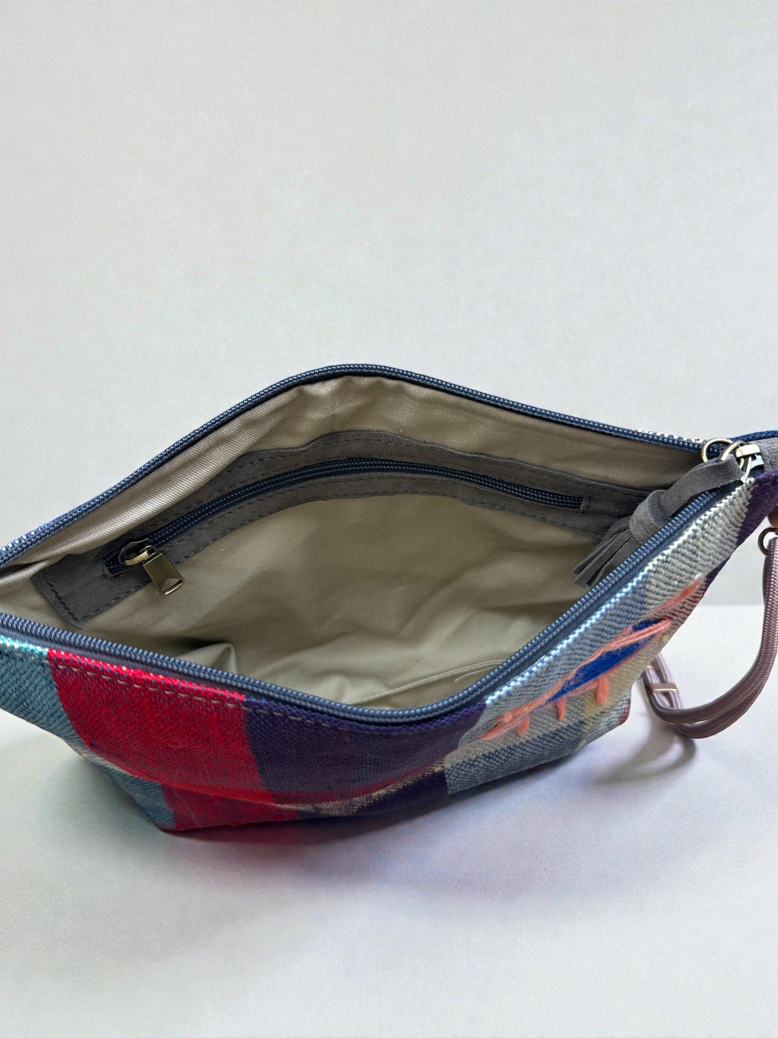 Die LEY! Tasche - OCULIA CLUTCH von LEY! hat ein rotes, blaues und graues Vintage-Stoff-Patchwork außen, ein beiges Innenfach mit Reißverschluss und einen braunen Trageriemen. Für Details offen abgebildet.