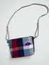 Die LEY! Tasche - OCULIA CLUTCH von LEY! ist eine kleine, rechteckige Umhängetasche aus Vintage-Stoff mit lila Träger, rot-blau-weiß kariertem Muster, gesticktem Auge vorne und "HEY"-Anhänger am Rand.