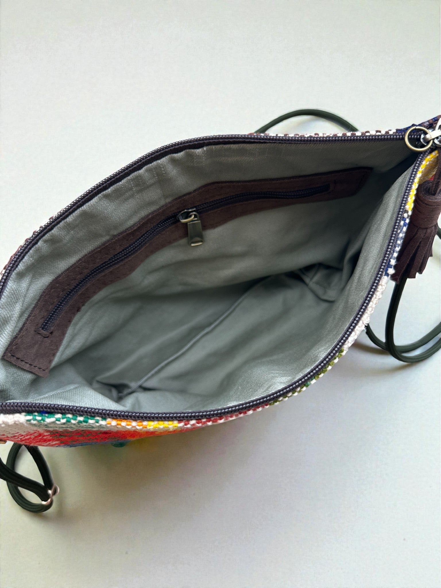 Die LEY! Tasche - OCULIA CLUTCH von LEY! ist eine kleine, handgefertigte Umhängetasche mit einer mehrfarbigen Außenseite, grauem Innenfutter und einer Innentasche mit Reißverschluss. Von oben betrachtet ist das leere Hauptfach gut sichtbar.
