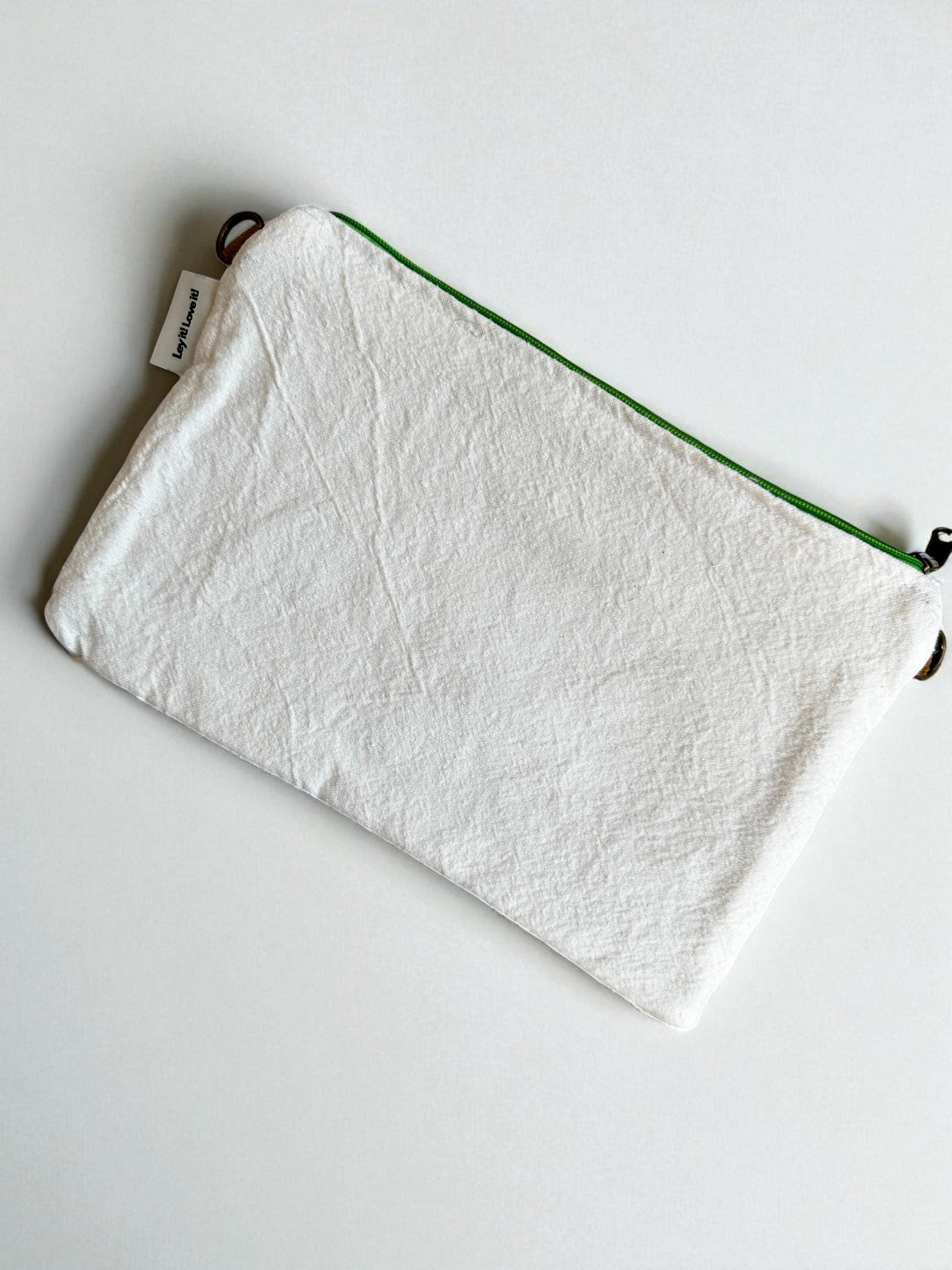 Eine rechteckige weiße Stofftasche mit einem neongrünen Reißverschluss und einem kleinen weißen Anhänger - die LEY! Tasche - Mona neongrün - 20x30cm ruht elegant auf einer schlichten weißen Oberfläche.