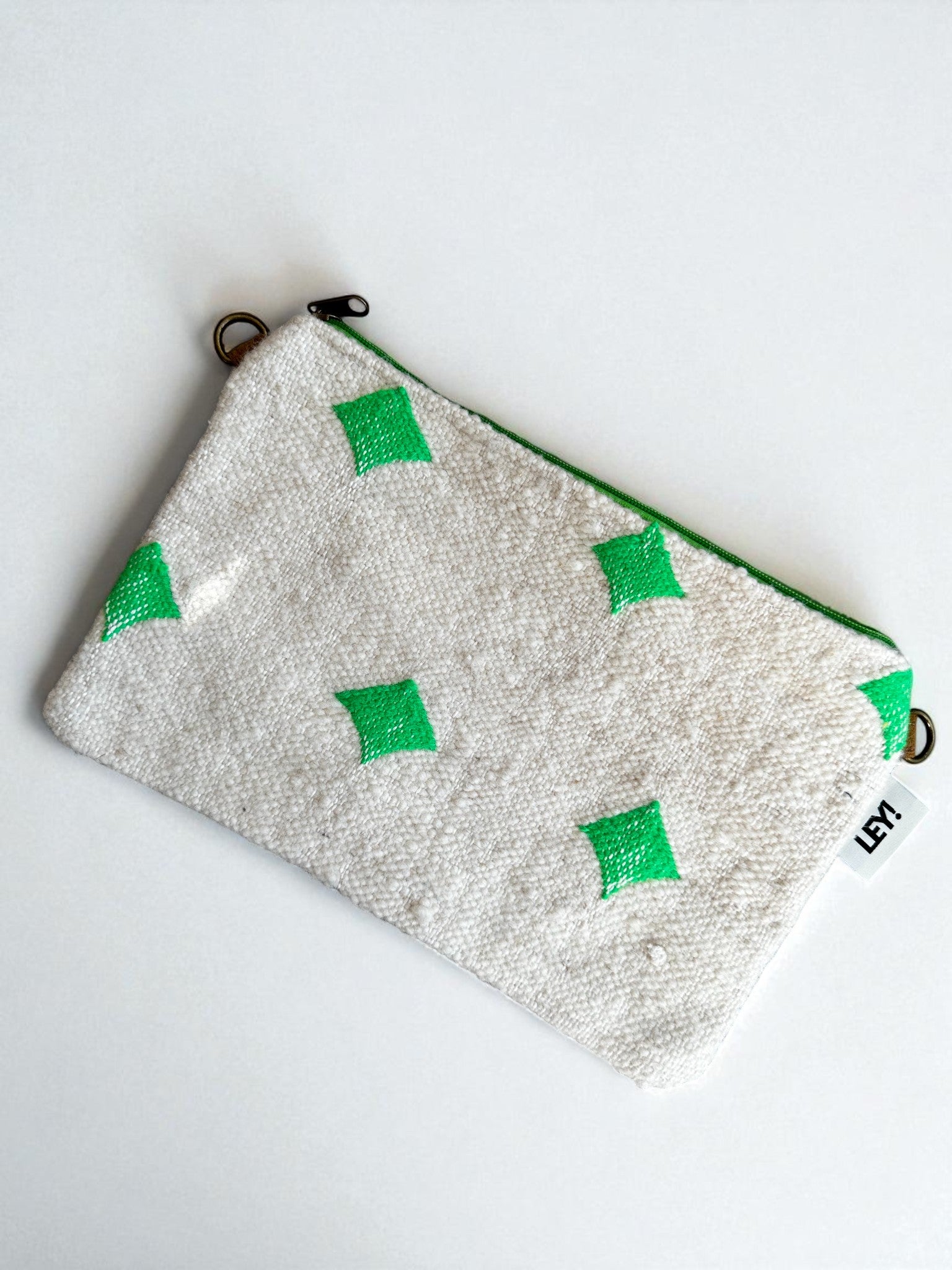 Die rechteckige weiße Tasche "Tasche - Mona neongrün - 20x30cm" von LEY! hat ein Streifendesign mit grünen Rauten, einen grünen Reißverschluss, Metallringe an jeder Seite und einen kleinen weißen "LEY!"-Anhänger. Es ist auf einem weißen Hintergrund abgebildet.