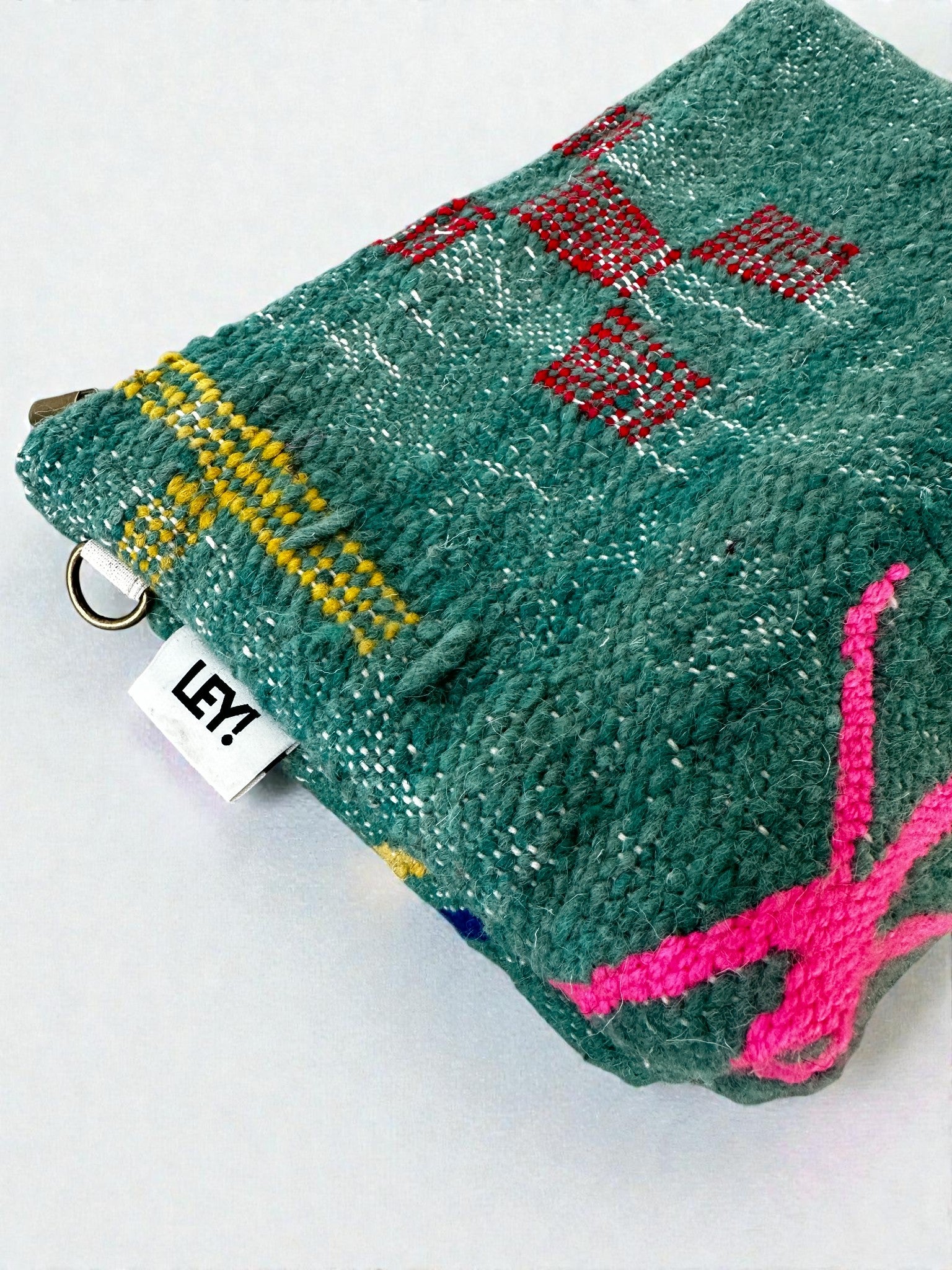 Die LEY! Tasche - Colorful Line (20 x 30 cm) ist eine strukturierte grüne Tasche mit roten, gelben und rosa Stickereien. Ein kleiner weißer "LEY!"-Schriftzug befindet sich neben einem Metallring, der die Handwerkskunst von Handarbeit Marrakesch unterstreicht.