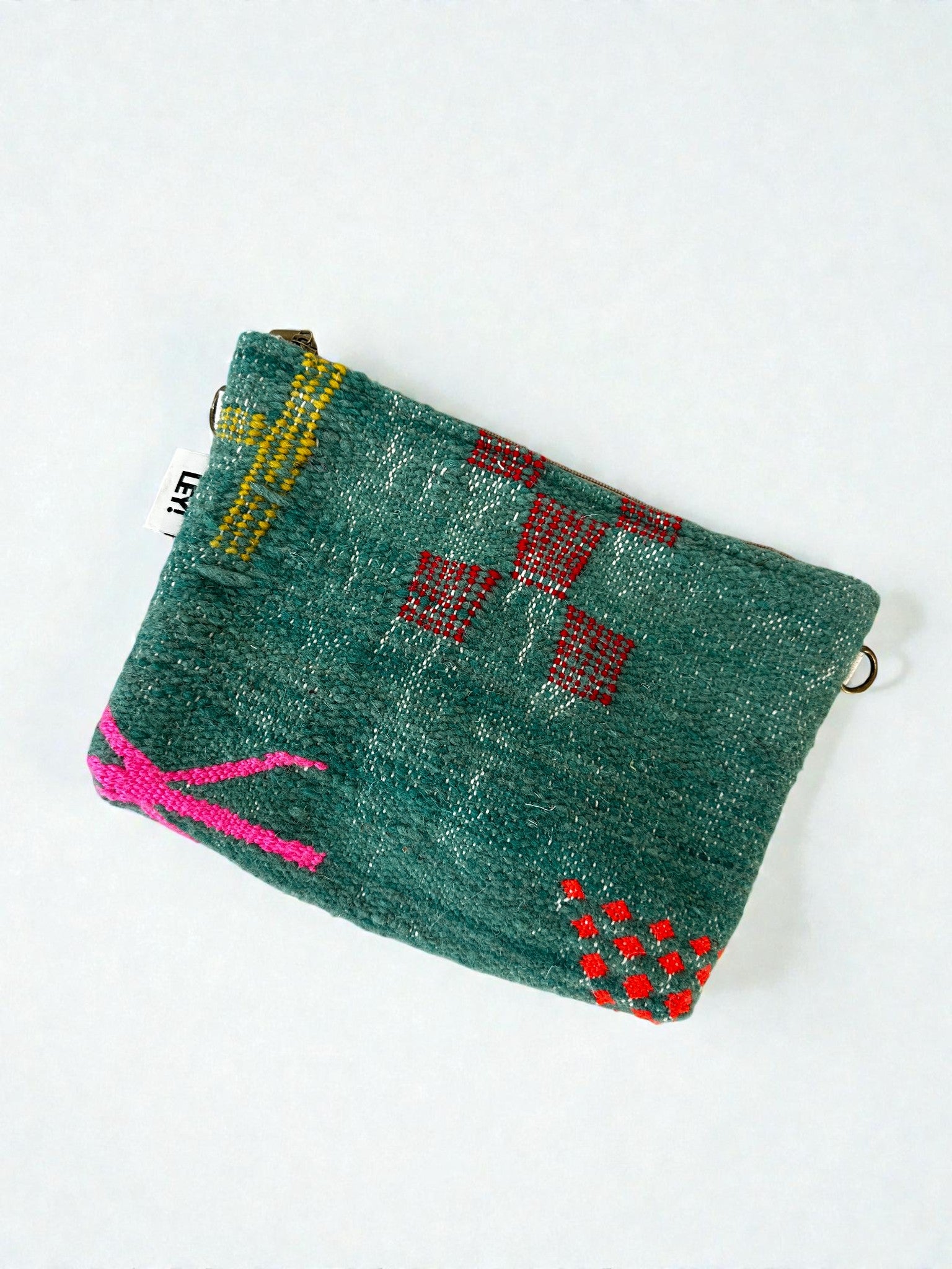 Die LEY! Tasche - Colorful Line (20 x 30 cm) ist eine kleine tealfarbene Wolltasche mit roten geometrischen Mustern, einem rosafarbenen Eckdesign, einem gelben Zickzack an der Oberseite, einem Reißverschluss und einem kleinen weißen Seitenanhänger.