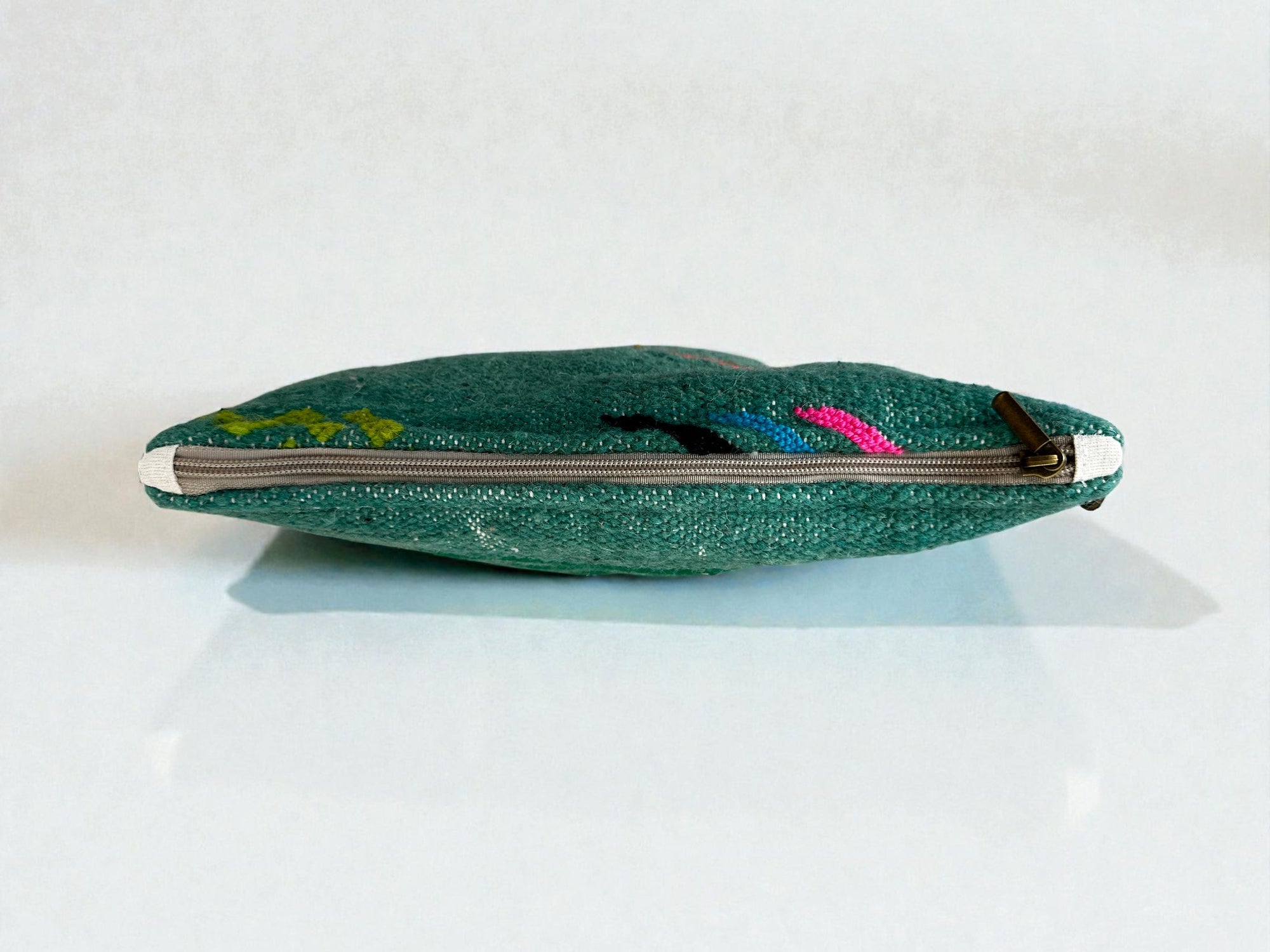 Die LEY! Tasche - Colorful Line (20 x 30 cm) ist eine flache grüne Reißverschlusstasche mit subtilen bunten Mustern und einer lebendigen Colorful Line, die von der Seite auf einer weißen Oberfläche gezeigt wird, wobei der Reißverschluss meist geschlossen ist.