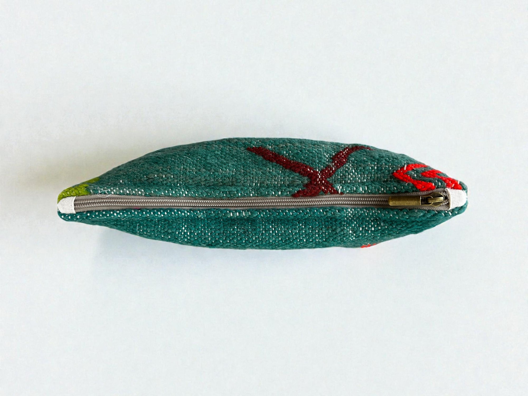 Eine kleine LEY! Tasche - Colorful Line (20 x 30 cm) in grüner Schurwolle, von oben gesehen mit geschlossenem Reißverschluss. Mit roten und gelben Handarbeits-Linienmustern im Marrakesch-Stil auf einfarbig weißem Hintergrund.