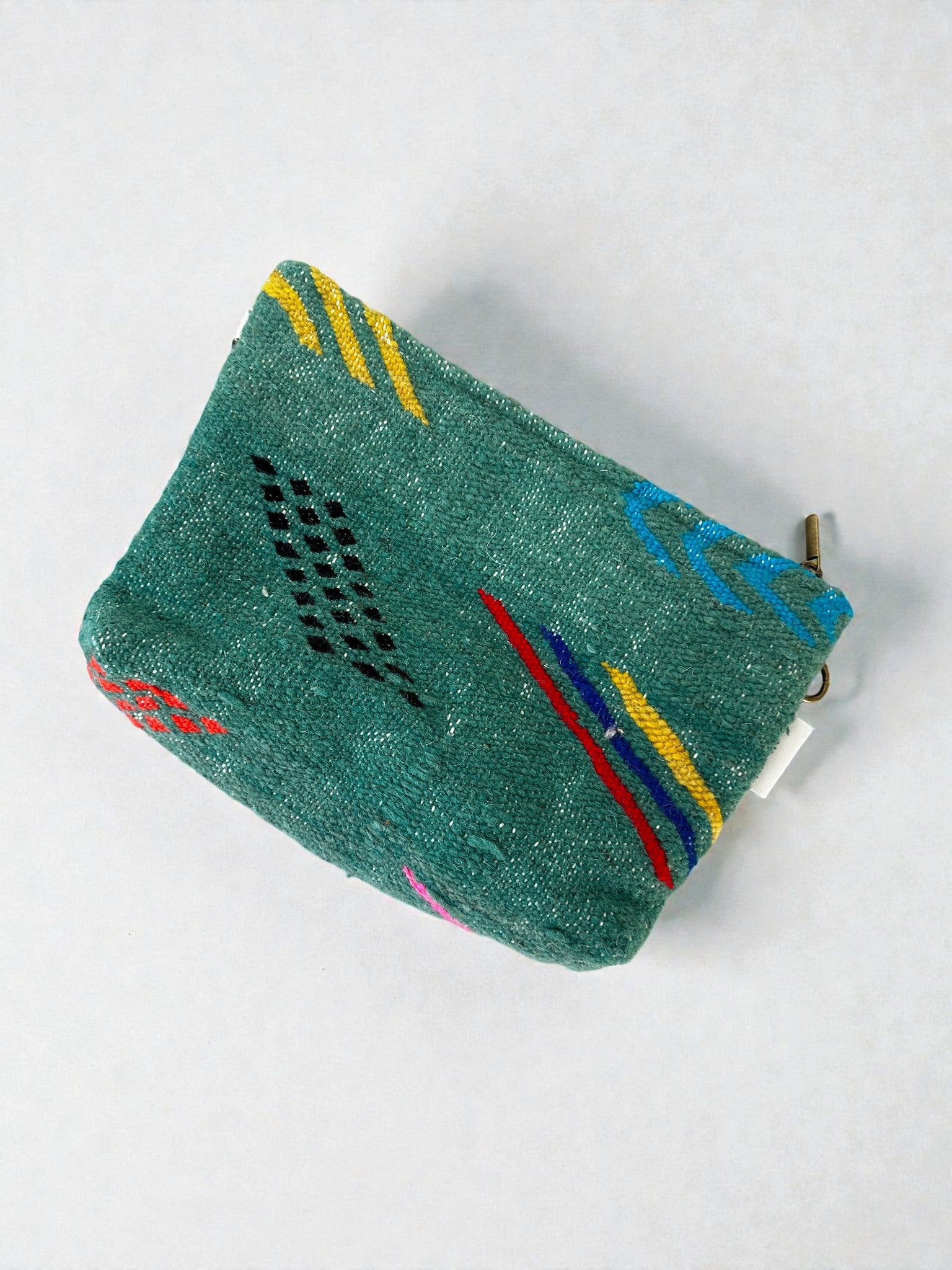 Eine kleine grüne LEY! Tasche - Colorful Line (20 x 30 cm) mit einem Reißverschluss, lebhaften geometrischen Mustern und bunten Akzenten ist auf einem einfarbig weißen Hintergrund abgebildet.