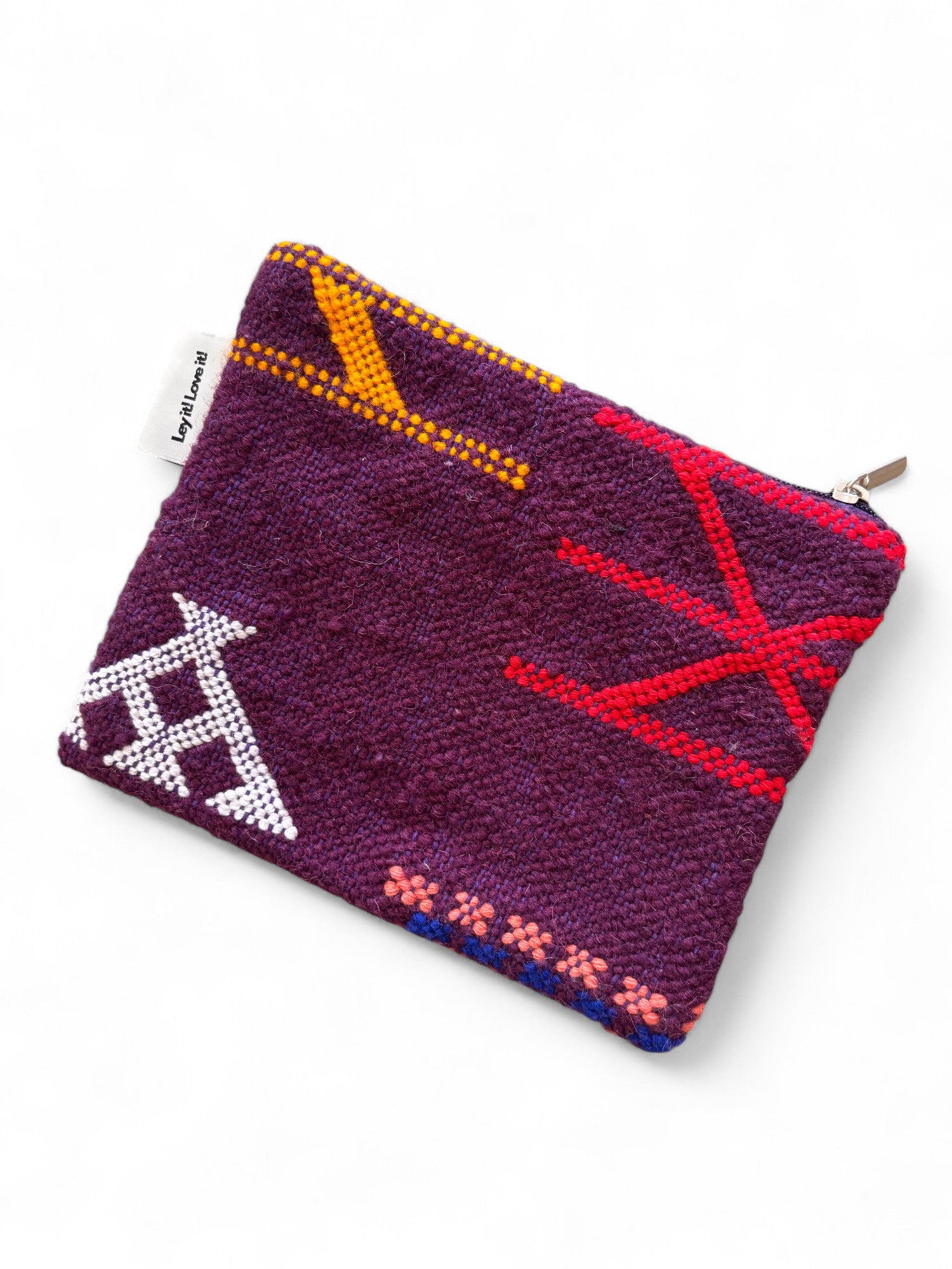 Die LEY! Tasche - Colorful Line - 15x20cm ist eine kleine, lila strukturierte Tasche mit Reißverschluss, die mit roten, gelben, weißen, rosa und blauen geometrischen Stickereien und einem seitlichen weißen Stoffanhänger versehen ist, inspiriert von Handarbeit Marrakesch.