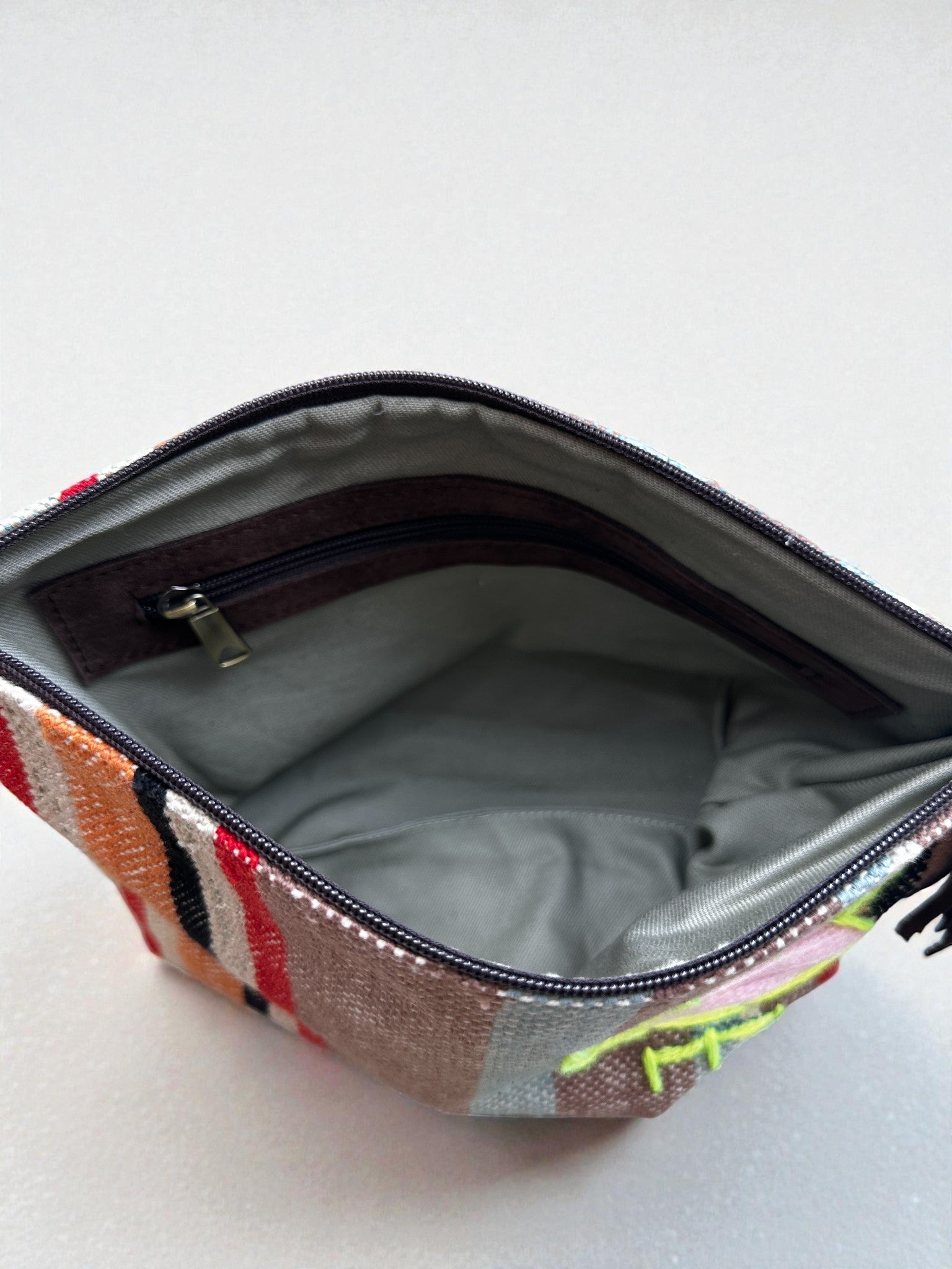Die LEY! Tasche - OCULIA CLUTCH von LEY! ist eine kleine Reißverschlusstasche aus Vintage-Stoff mit grauem Innenfutter, einer Innentasche mit Reißverschluss und einem bunten abstrakten Muster. Die offene Tasche hebt ihr schickes Innenleben hervor.