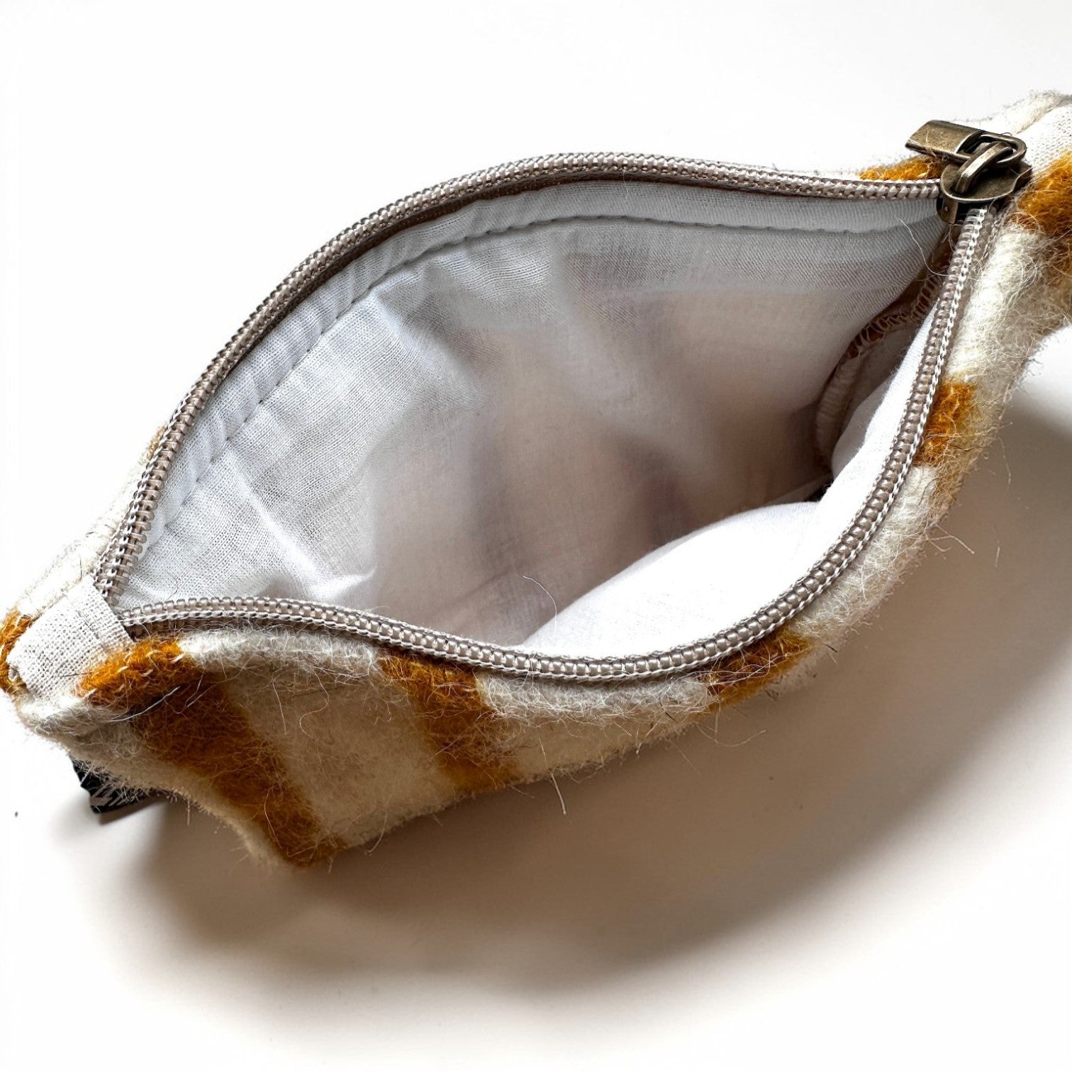 Ein kleines Täschchen mit weiß-braun gestreifter Außenseite, weißem Innenfutter und Metallreißverschluss - das ist die LEY! Tasche - WINTER EDITION - SONNE (15 x 20 cm), Teil der Handarbeit Marrakesch Winter Edition.