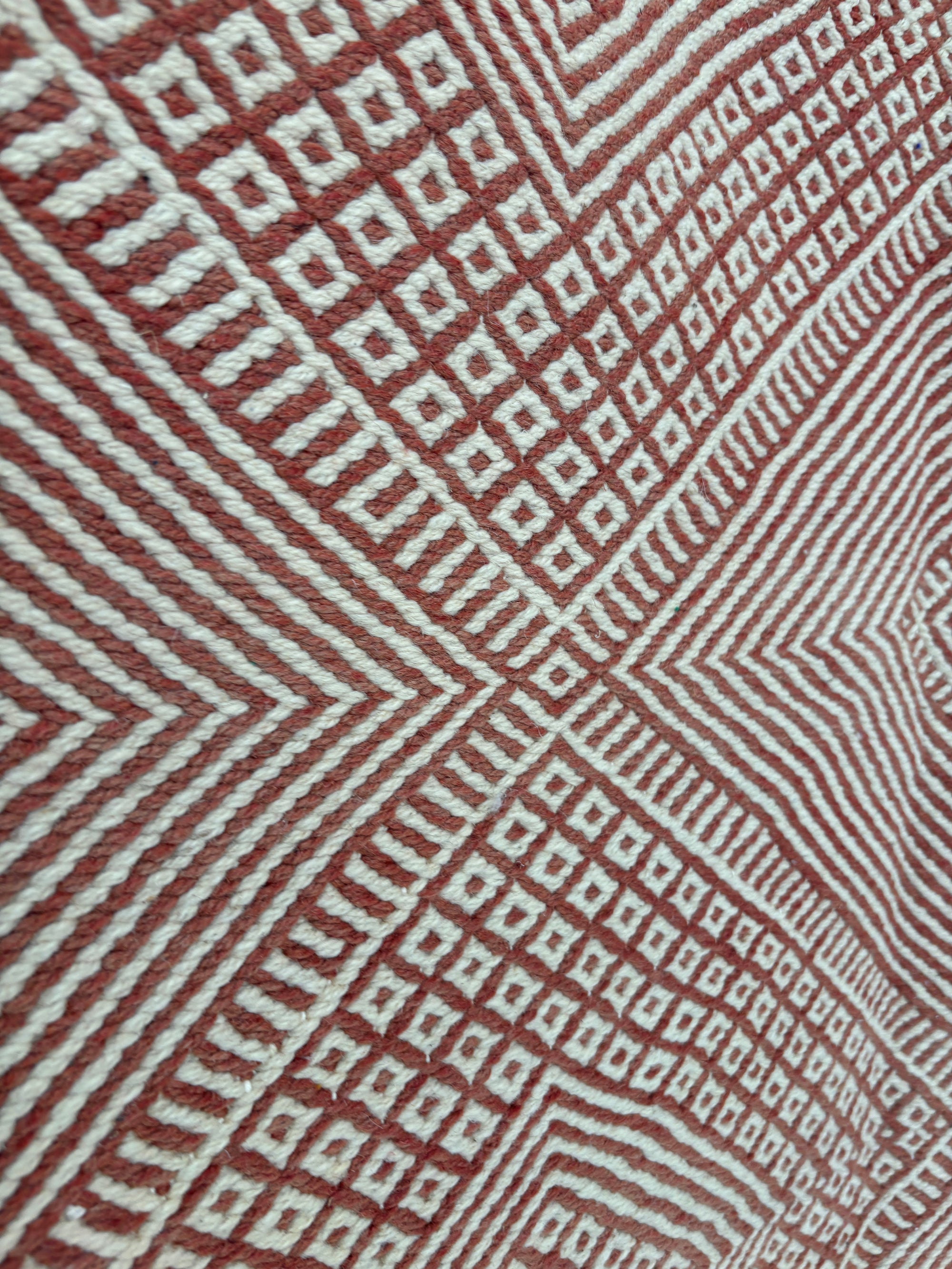 Eine Nahaufnahme des LEY Teppichs "Sonia" 1,95 x 3,00 von LEY! zeigt einen flachgewebten Teppich mit einem rot-weißen, geometrischen Muster aus konzentrischen Rauten und kleinen Quadraten, das für einen kräftigen, symmetrischen Look sorgt.
