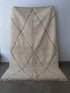 Der BERBER TEPPICH "ILAJHA" von LEY! (2,00 x 3,00 m) ist ein cremefarbener, handgeknüpfter Berberteppich aus naturbelassener Wolle mit zotteliger Struktur, schlichtem schwarzen Rautenmuster und Fransen an der Unterkante.