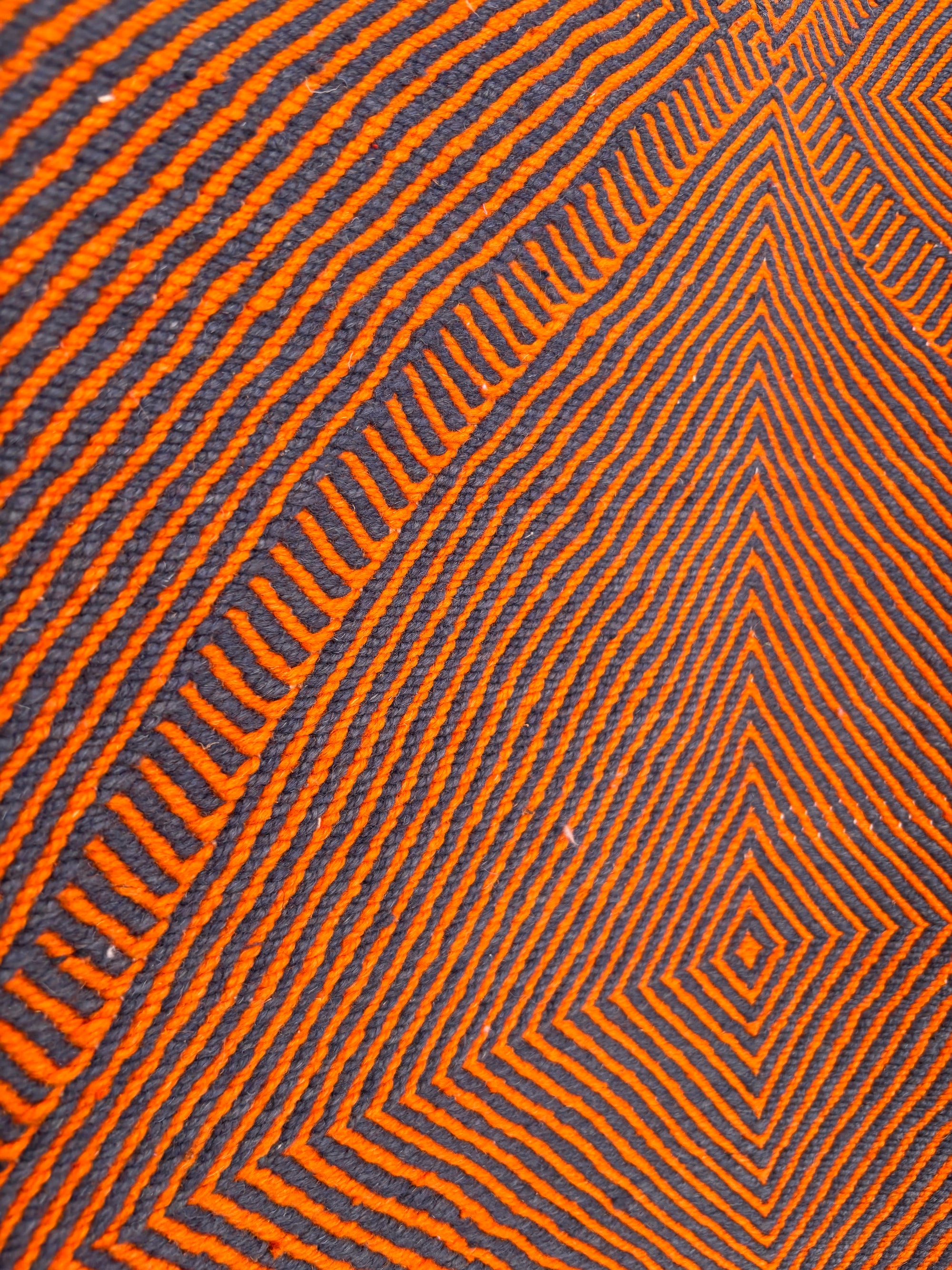 Nahaufnahme des LEY-Teppichs "Rabina" 2,00 x 3,00 von LEY! mit orangefarbenen Linien, die geometrische Formen und konzentrische Rauten auf einem dunklen Hintergrund bilden und einen optischen Täuschungseffekt erzeugen.